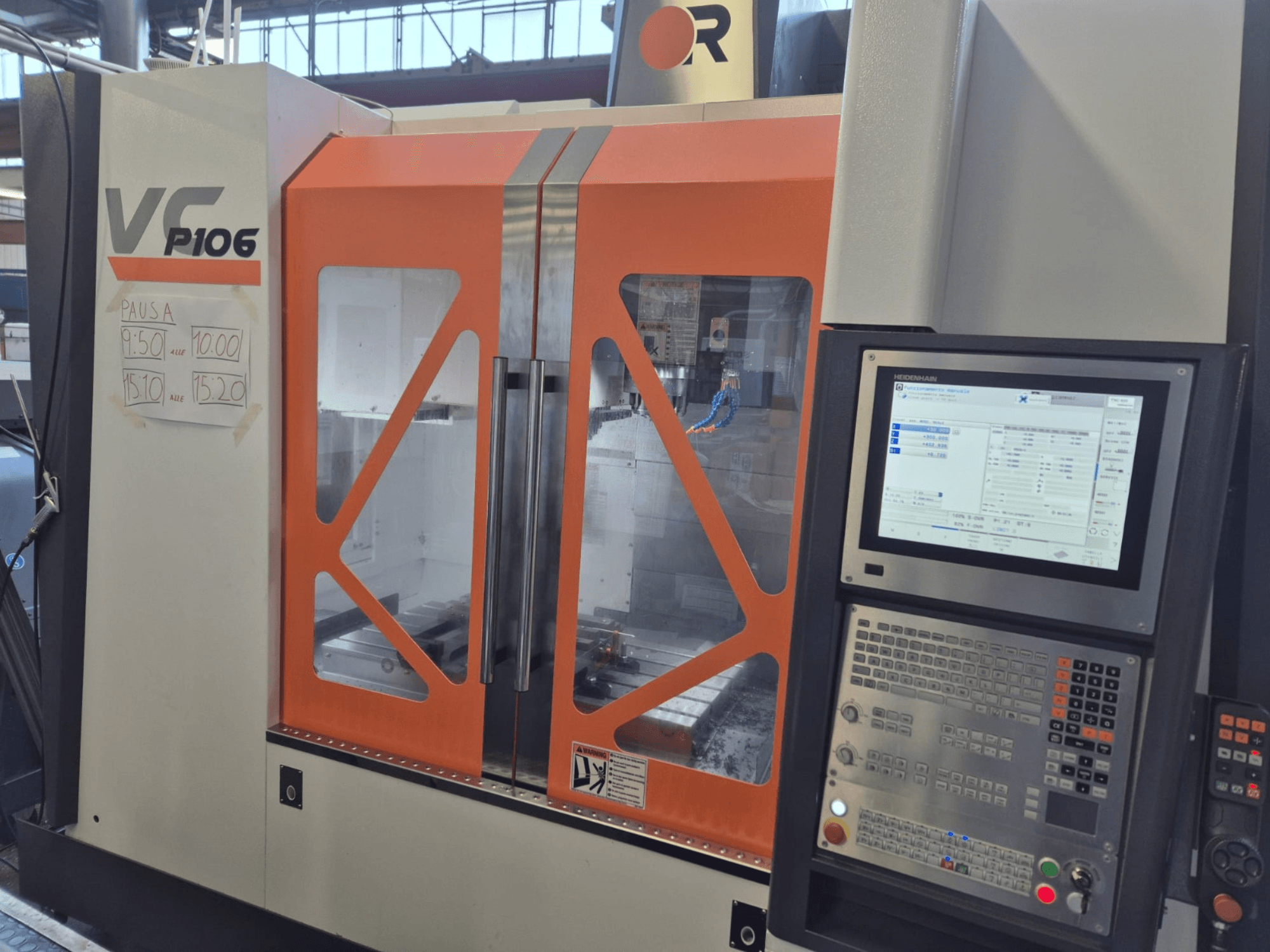Testo Alt: Macchina CNC VF P106 arancione e grigia, vista frontale, con pannello di controllo e tempi di funzionamento programmati su carta.
