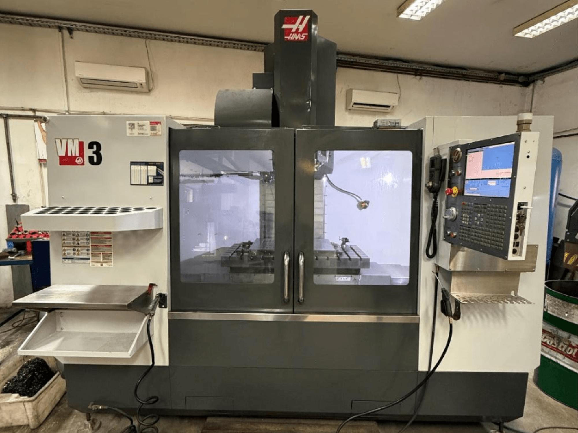 Centro di lavorazione verticale Haas VM-3 in vista frontale, dotato di un ampio pannello di controllo e di un'area di lavoro visibile con gli utensili.