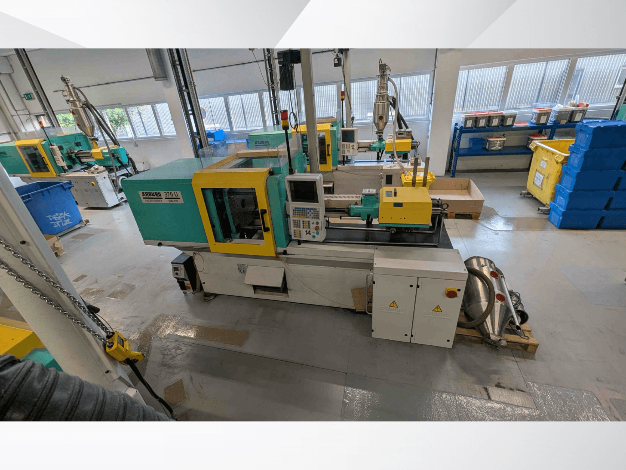 Vista frontale della pressa a iniezione verticale Arburg 370 U 500-170 con pannello di controllo e componenti della macchina all'interno di un'officina.