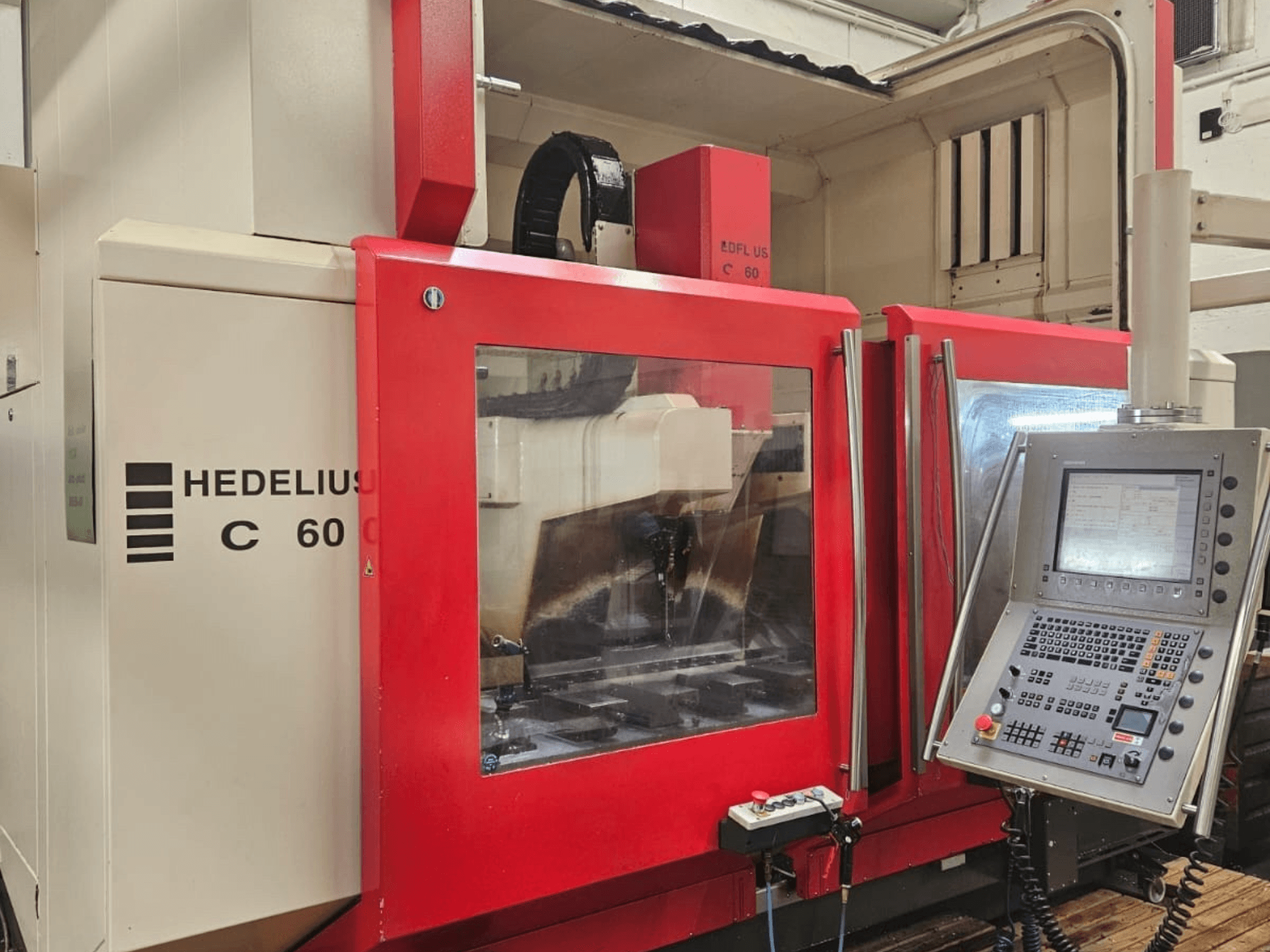 Centro di lavoro verticale HEDELIUS C60 visto di lato, con pannello frontale rosso e console di controllo con display.