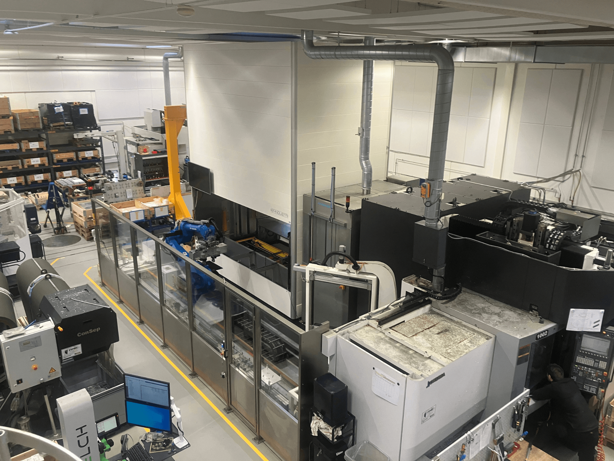 Sistema di automazione SSI SCHAFER Logimat in un magazzino, vista frontale; presenta braccio robotico, scaffalature di stoccaggio e macchinari.