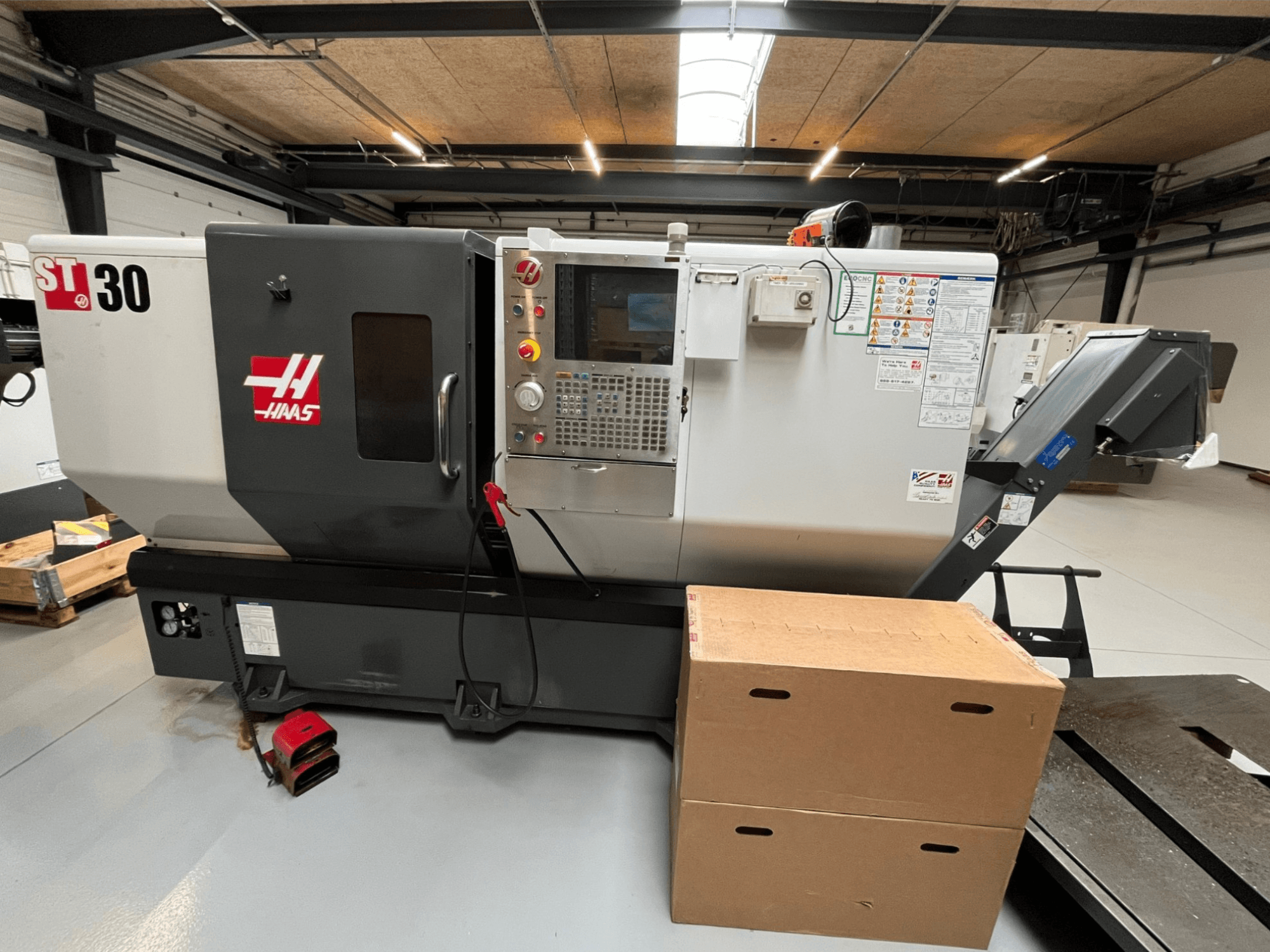 Tornio CNC Haas ST-30, vista frontale, pannello di controllo con pulsanti, arresto di emergenza e due scatole di cartone impilate.