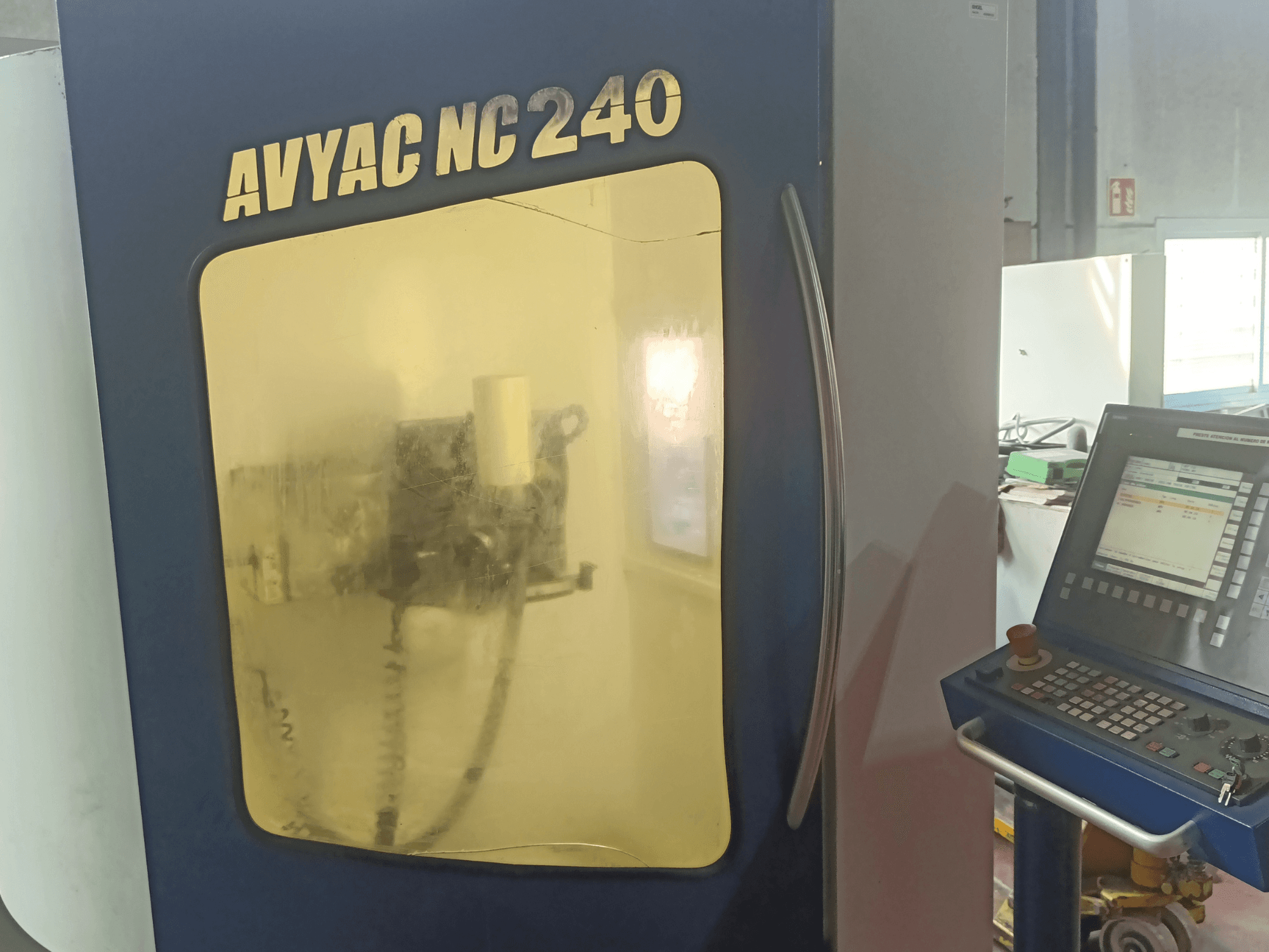 Rettificatrice cilindrica AVYAC NC240, vista laterale che mostra il pannello di controllo e l'area di rettifica parzialmente visibile attraverso la finestra.