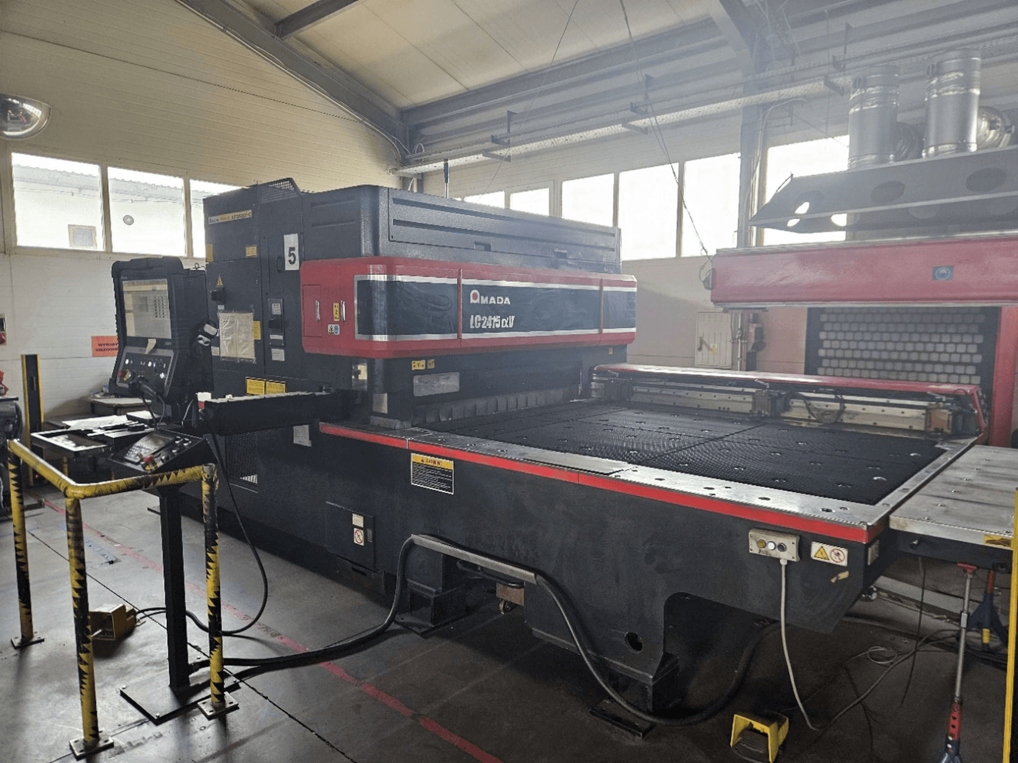 Macchina per il taglio laser a CO₂ AMADA LC2415 Alpha 5, vista frontale che mostra il pannello di controllo e il piano di taglio con le barriere di sicurezza.