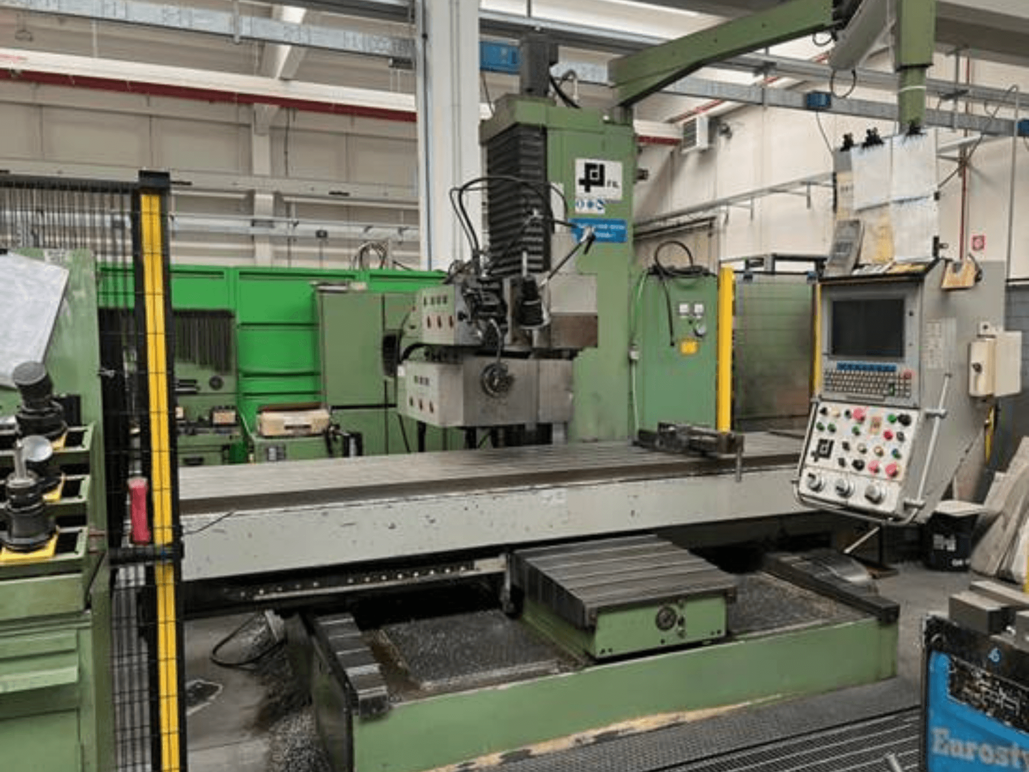 Fresatrice industriale JFL, vista frontale con pannello di controllo, grande tavolo piatto e trucioli di metallo sul pavimento.