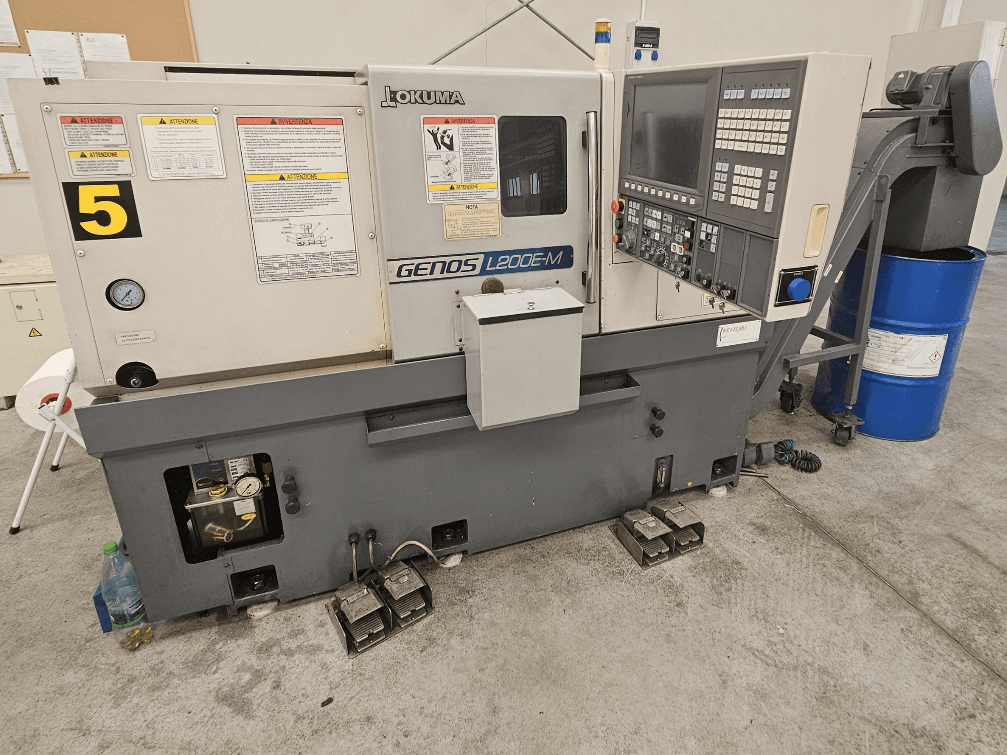 Tornio orizzontale Okuma GENOS L200E-M in vista frontale, con pannello di controllo, etichette e barilotto del refrigerante.