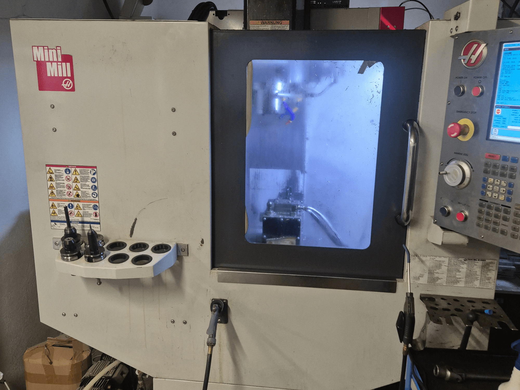 Vista frontale della Mini Mill HAAS, che mostra il pannello di controllo, i portautensili e la vista dell'area di lavorazione con il refrigerante.