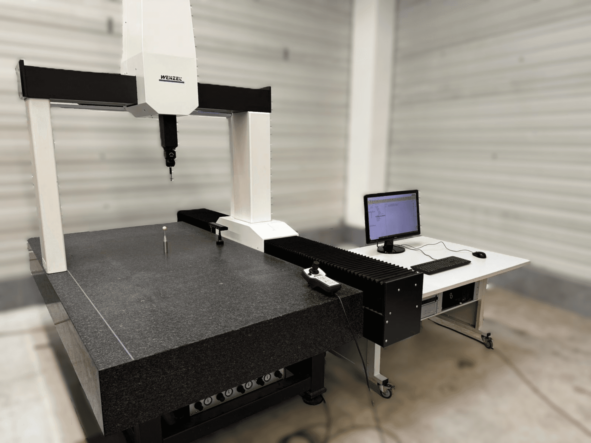 La CMM Wenzel XO 87 in una vista frontale, con una sonda di misura e un tavolo di granito con un computer accanto.