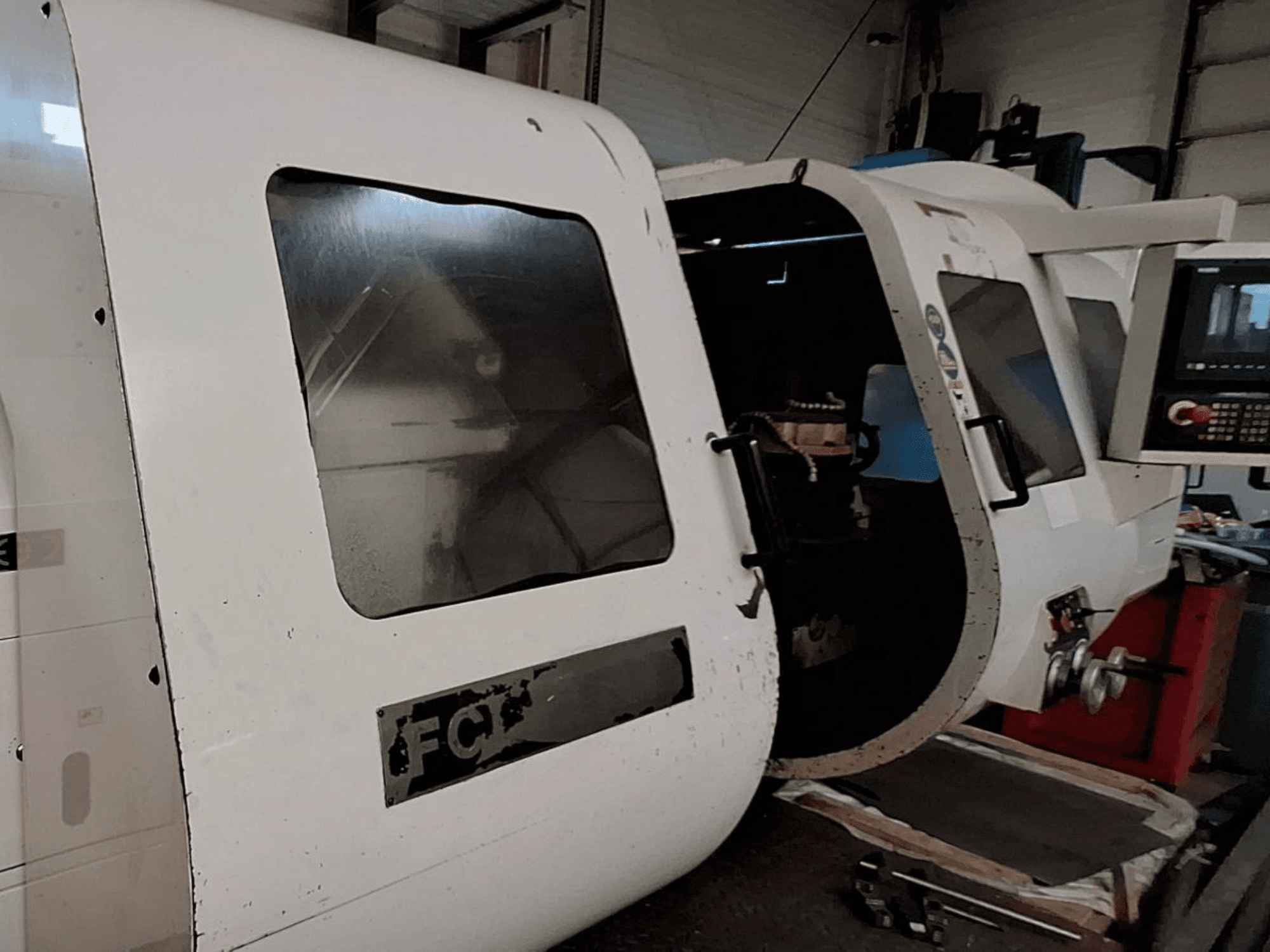 Macchina CNC bianca con pannello di controllo visibile e porta aperta, che mostra i componenti interni; vista frontale. Marchio: FCT.