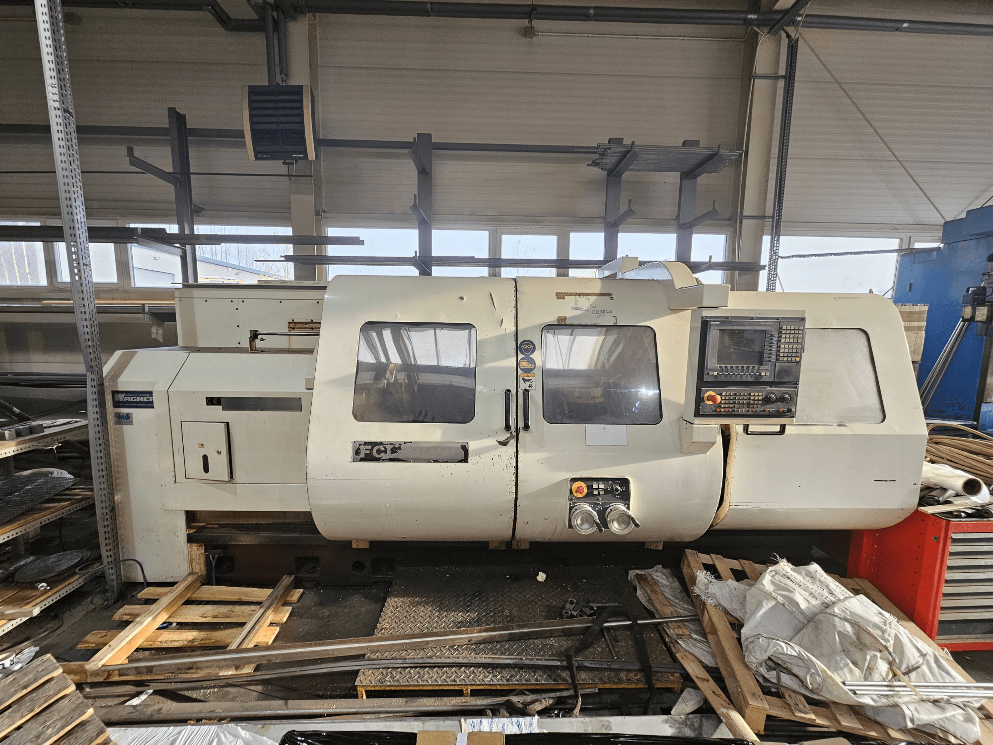 Tornio CNC Wabeco, vista laterale, con pannello di controllo, finestre e area di lavoro; macchinari su pallet di legno in un'officina.