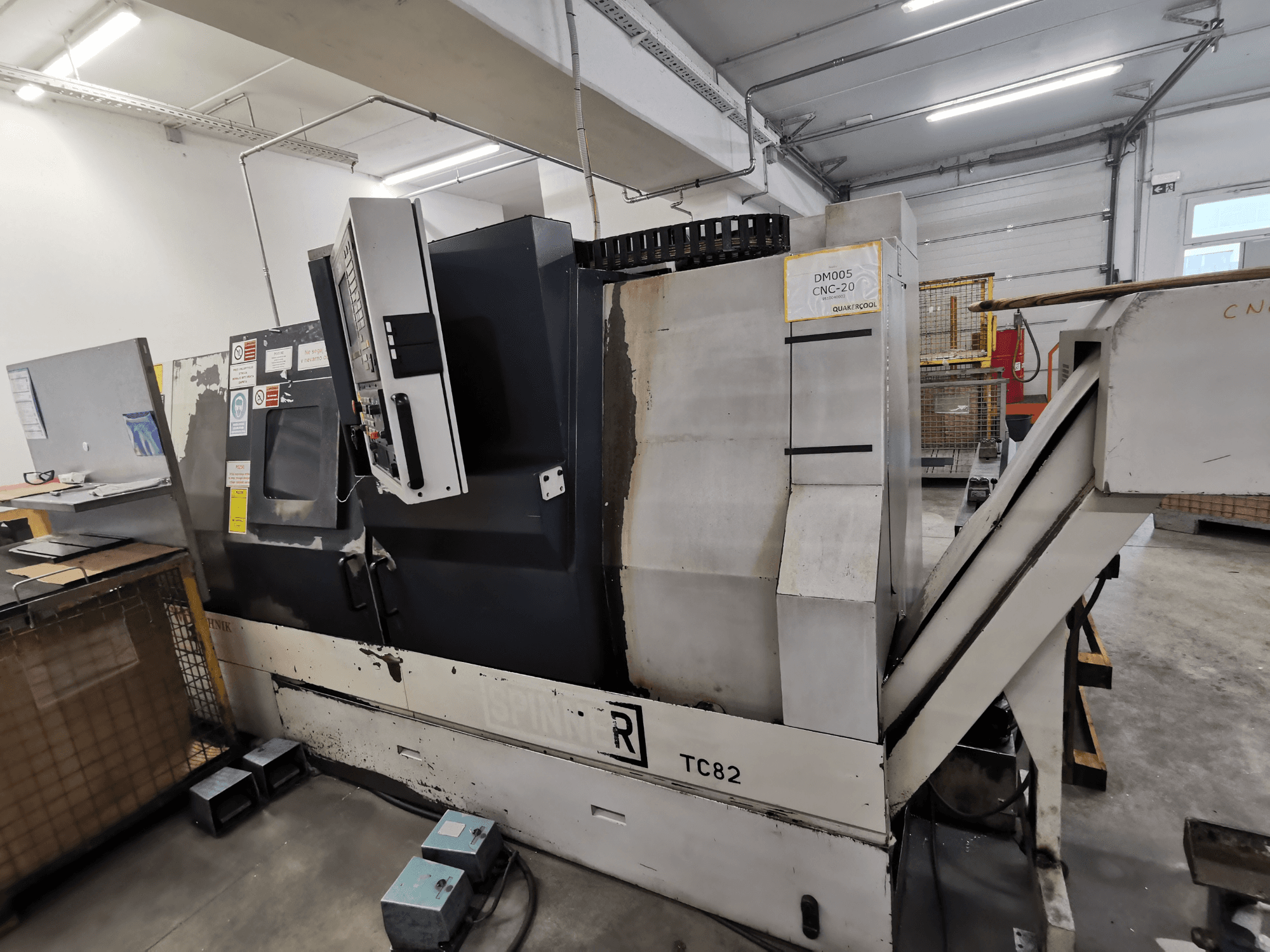 Macchina CNC, marca Spinner, modello TC82, vista laterale che mostra il pannello di controllo e lo scivolo di rimozione degli scarti in un'officina.