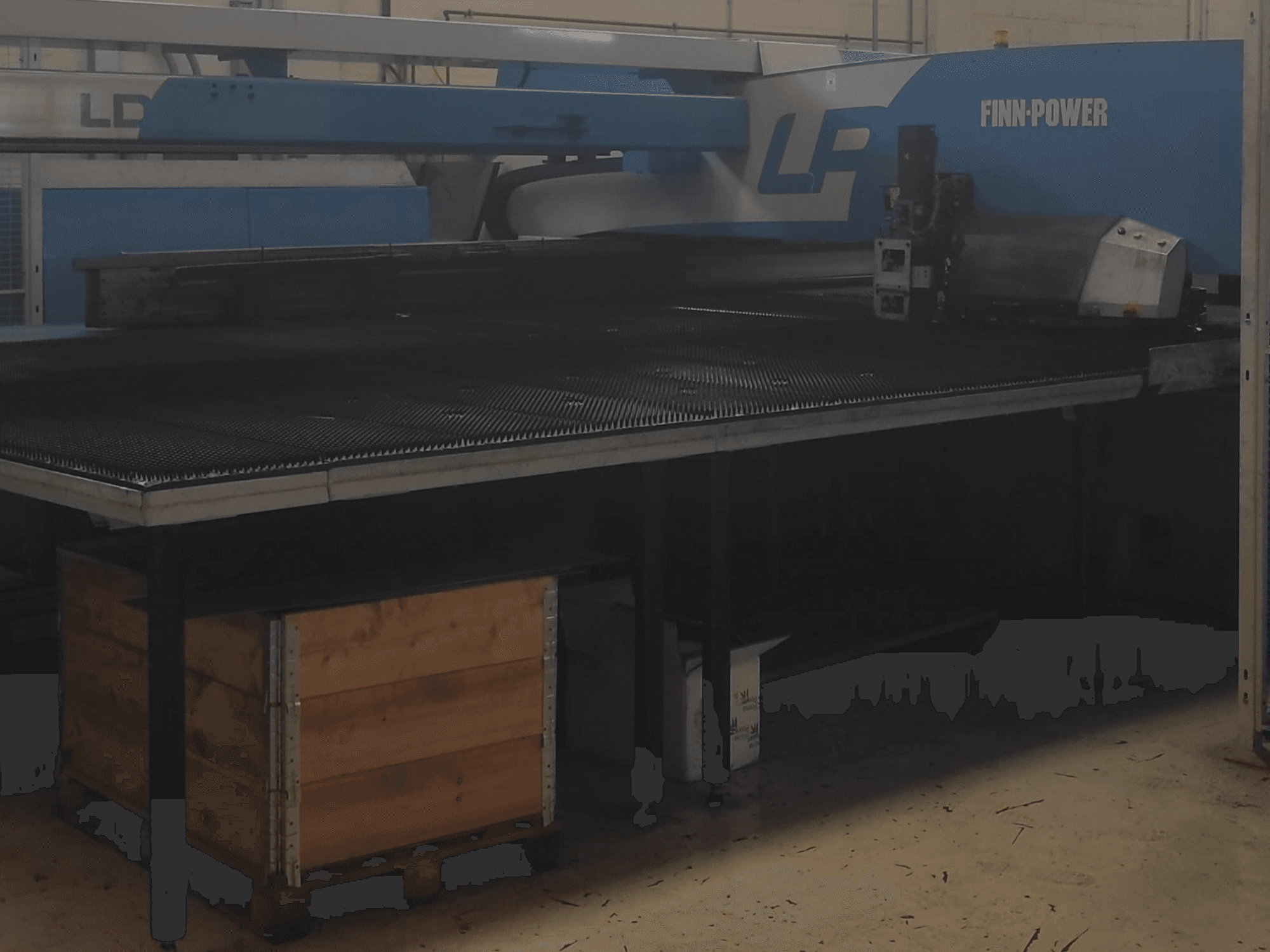 Macchina da taglio Finn-Power LP in una fabbrica, vista frontale con tavolo in metallo strutturato e cassa di legno sottostante.