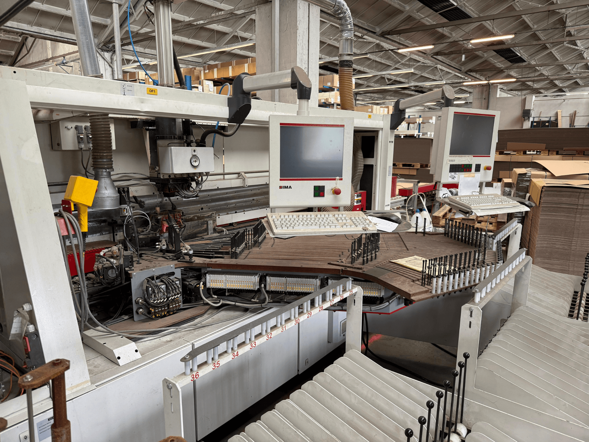 Macchina di precisione IMA per la lavorazione del legno con doppio monitor e pannelli di controllo, vista frontale che mostra il trasportatore e l'area degli utensili.