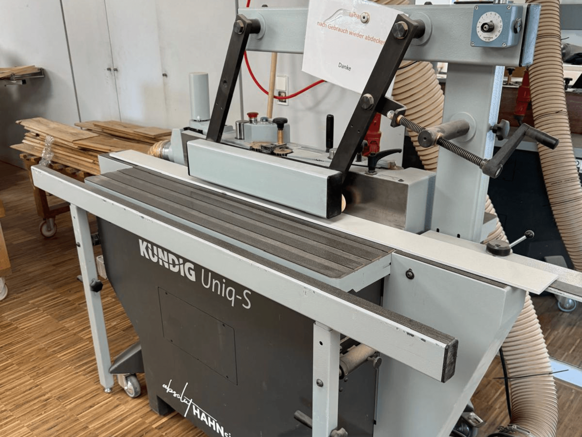 Levigatrice a nastro Kundig UNIQ-S in un'officina, vista laterale che mostra il nastro abrasivo e i bracci di supporto regolabili.