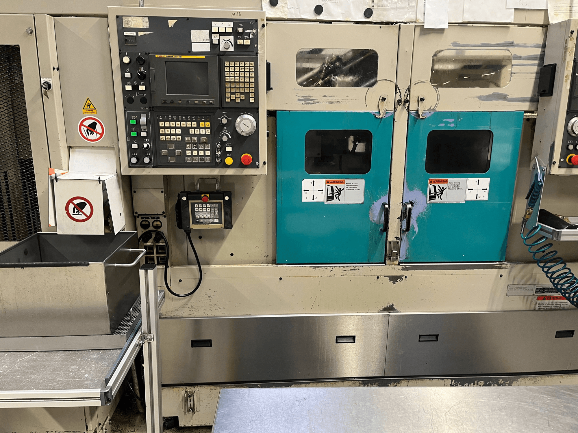 Pannello di controllo di una macchina di produzione con porte di colore verde, avvisi di sicurezza e tastiera; vista frontale, finitura in acciaio inox.