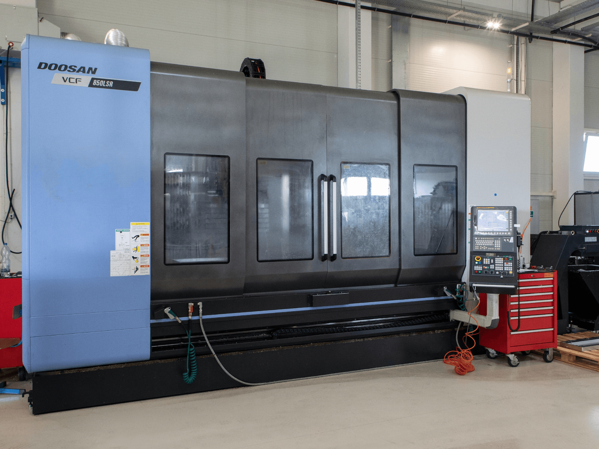 Centro di fresatura e tornitura DOOSAN VCF850, vista frontale; dotato di ampie finestre doppie, pannello di controllo e vano porta-utensili. Ideale per la lavorazione meccanica.