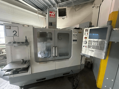 Macchina CNC Haas VF-2, vista frontale, con comandi, portautensili e porte trasparenti con utensili visibili all'interno dell'armadio.