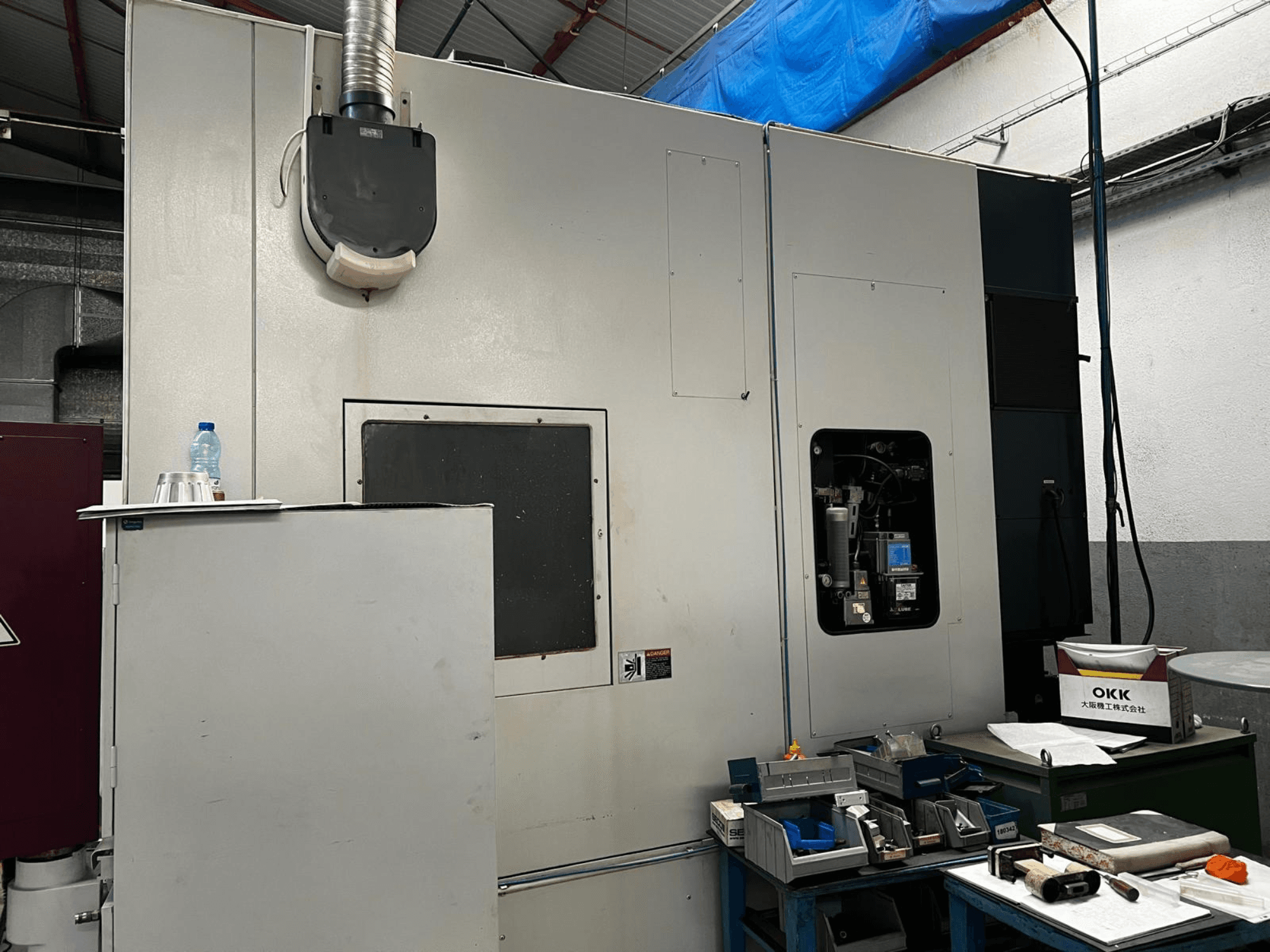 Centro di lavorazione verticale OKK VP600 in un'officina; vista laterale che mostra i dettagli della macchina e gli utensili su un tavolo adiacente.