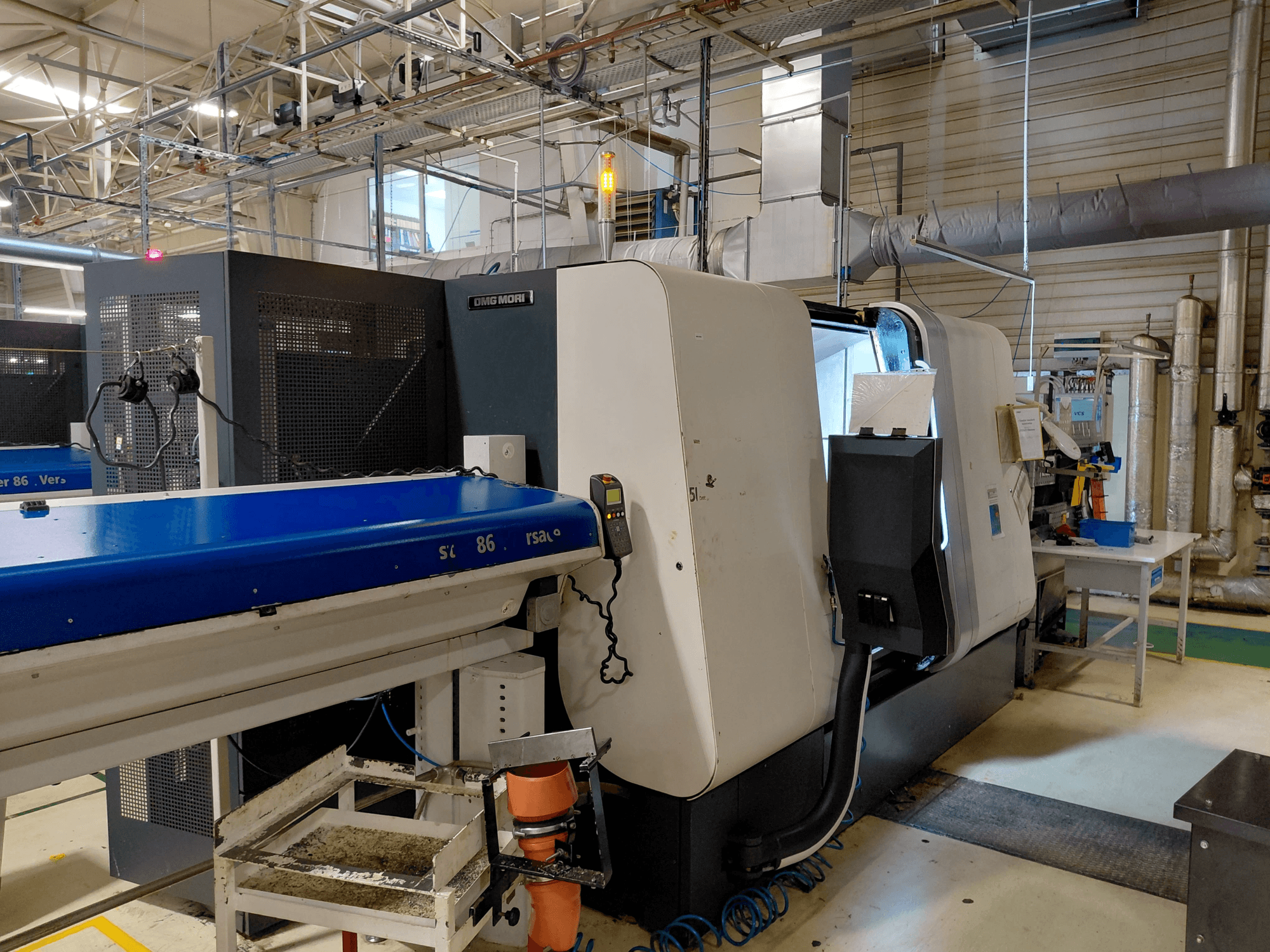 Tornio multimandrino lineare DMG MORI Sprint 65, vista laterale con pannello di controllo e trasportatore visibili in un'officina.