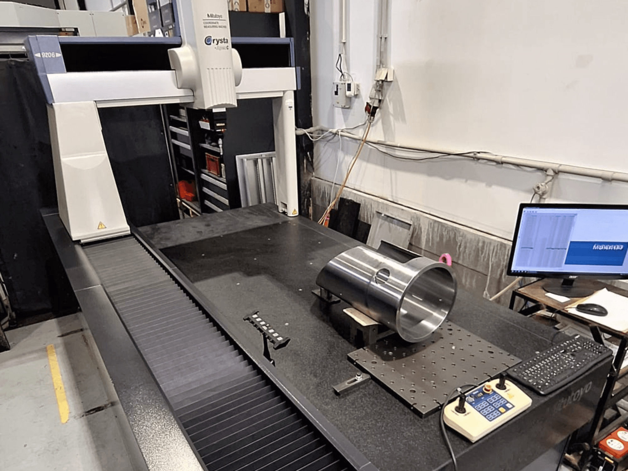 La CMM Mitutoyo Crysta-Apex C9206 in vista frontale, mentre misura un pezzo cilindrico in metallo su una piastra di granito nero.