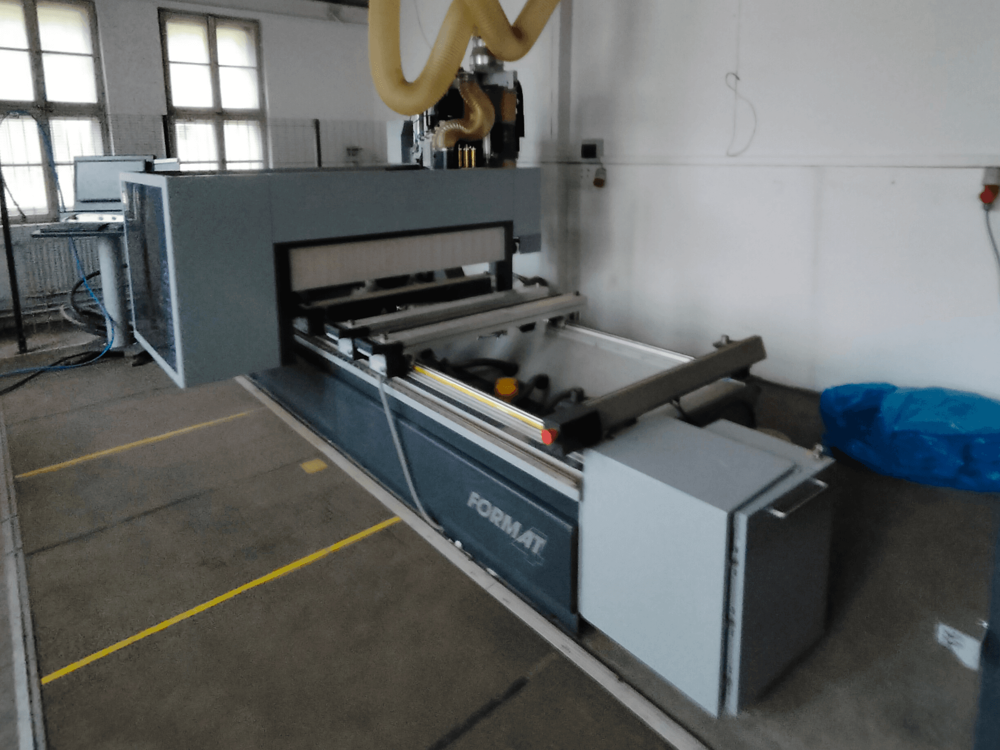 Vista frontale di una macchina CNC Format con corpo grigio, dotata di guide e di un pannello di controllo visibile.