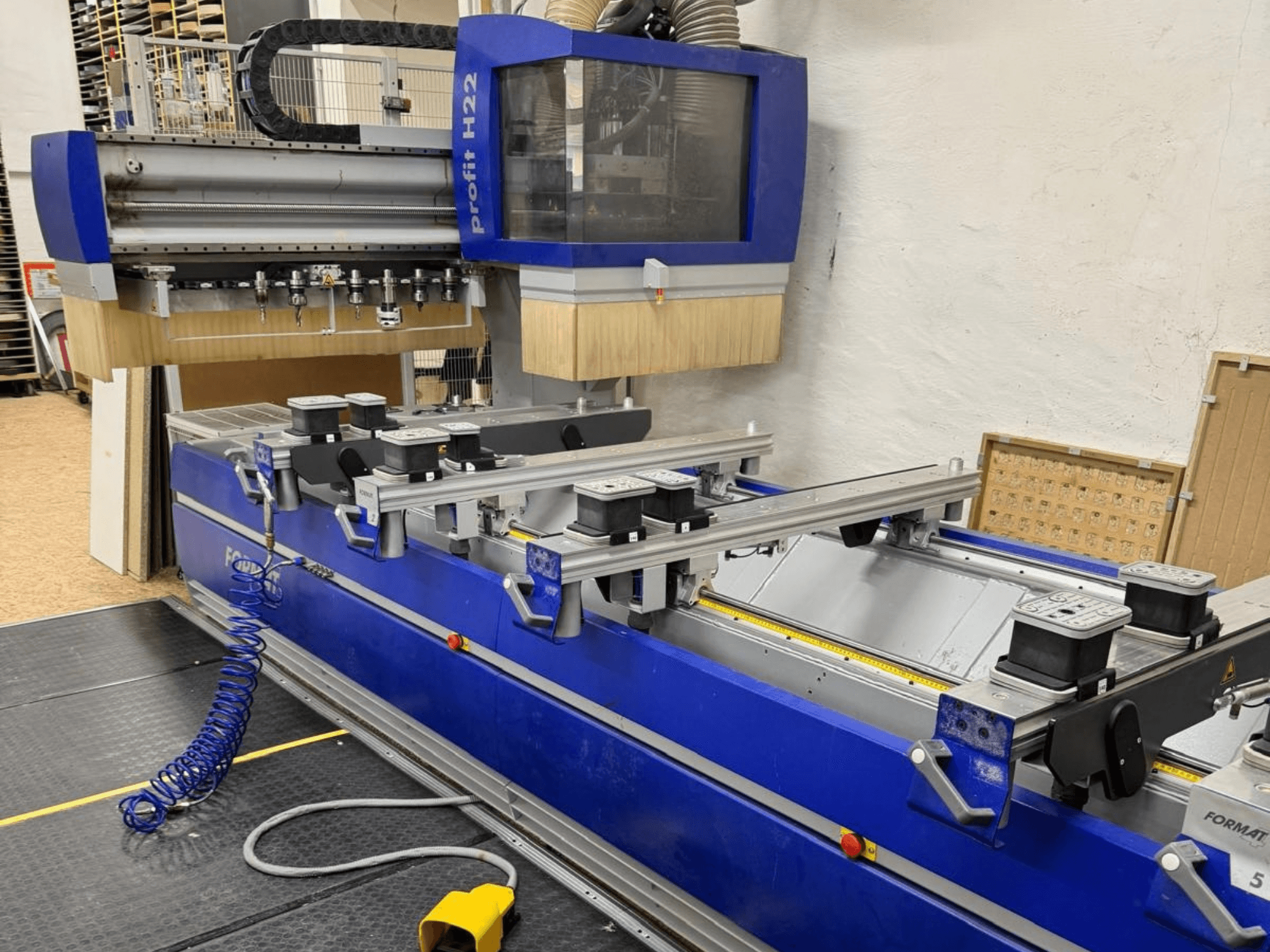 Centro di lavorazione del legno CNC FORMAT4 PROFIT H22, vista frontale, con utensili di lavorazione e morsetti di fissaggio visibili sul corpo blu.