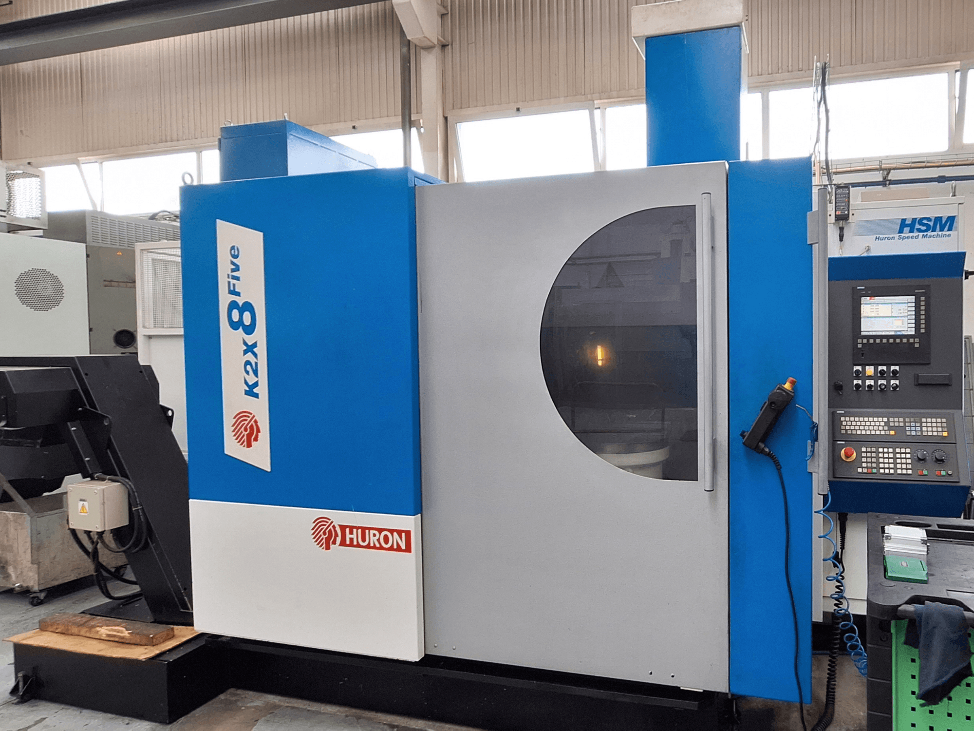 Fresatrice a portale Huron K2X 8 Five, vista frontale che mostra il pannello di controllo e l'ampia finestra di osservazione.