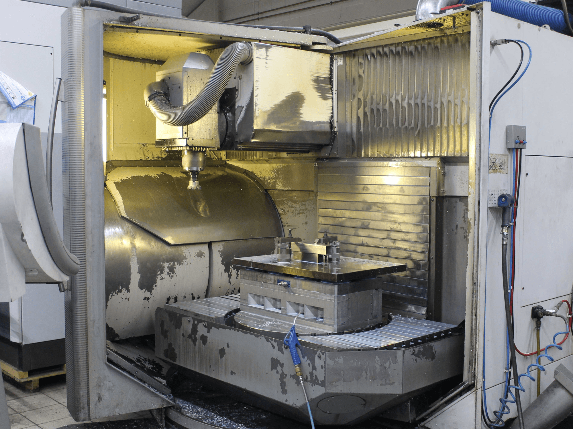 Interno di una fresatrice CNC, vista laterale, che mostra il pezzo e l'utensile da taglio con trucioli di metallo e residui di refrigerante.