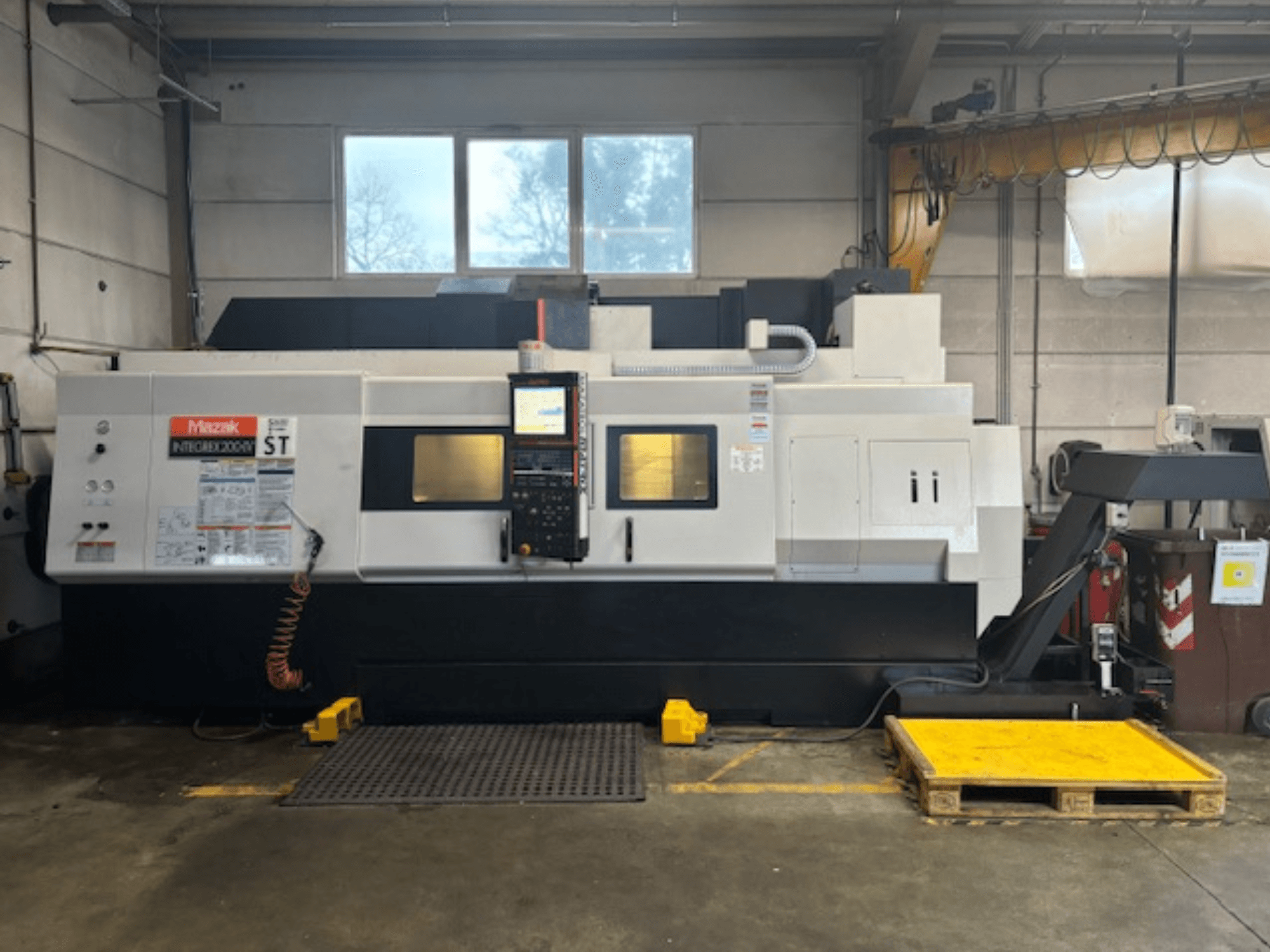 Mazak Integrex 200 SY ST, vista laterale, che mostra il pannello di controllo, i display operativi e le linee del refrigerante in un'officina.