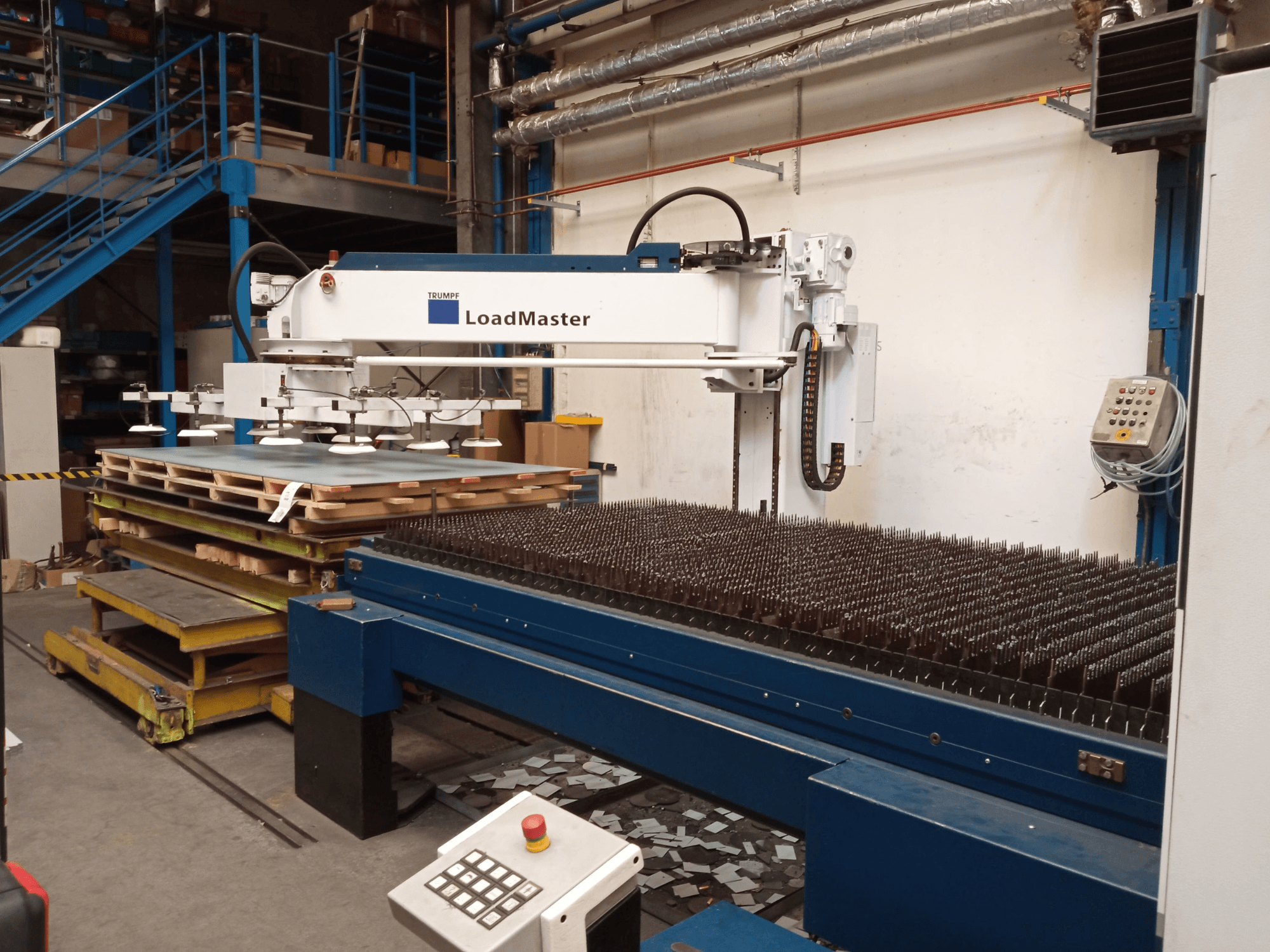 Macchina per il taglio laser a CO₂ TRUMPF TruLaser 3030 vista di profilo, dotata di un LoadMaster e di pallet di materiali.