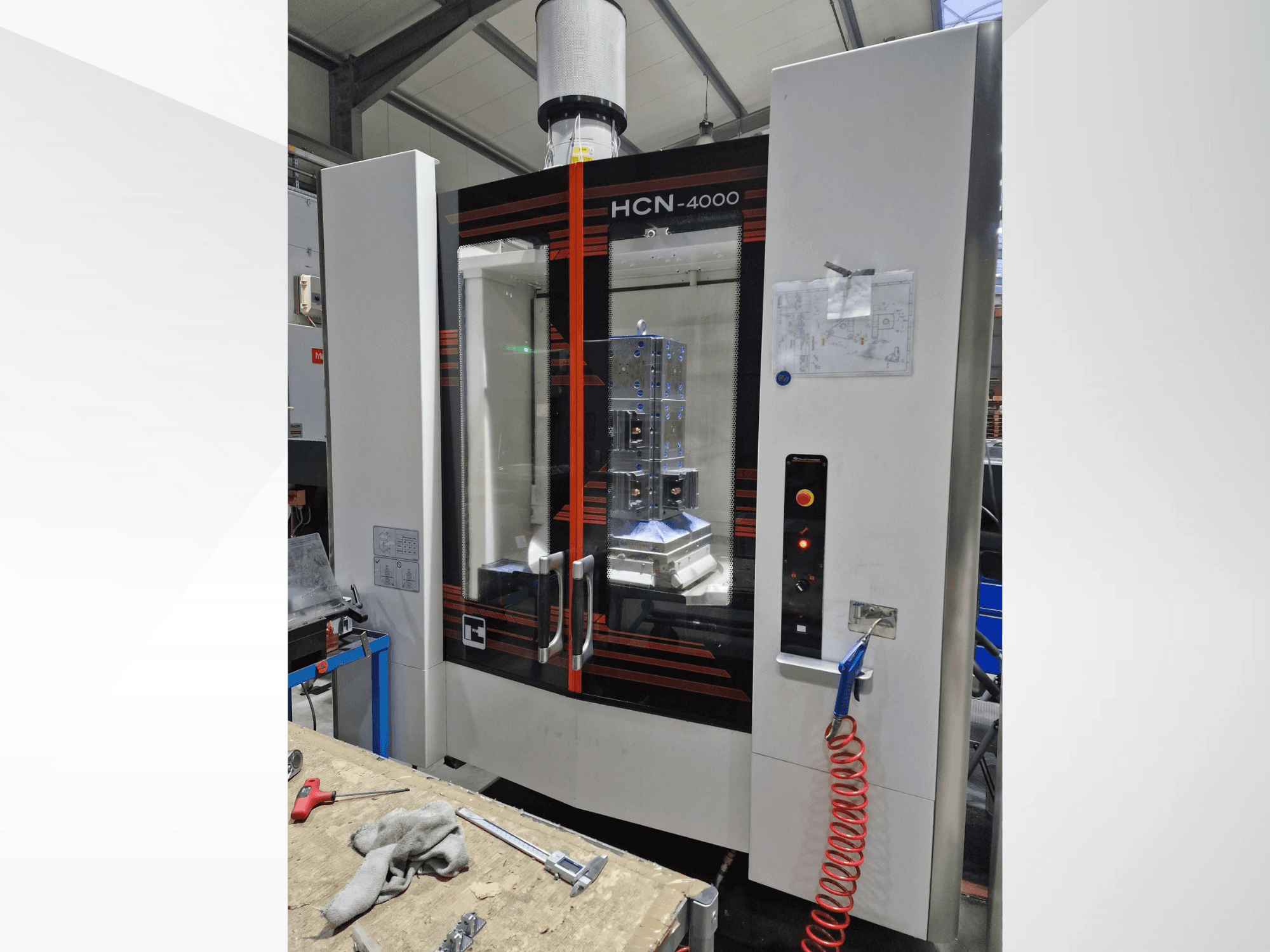 Macchina CNC HCN-4000 in vista frontale, con un pannello di vetro, un pannello di controllo con pulsanti e una cianografia allegata.