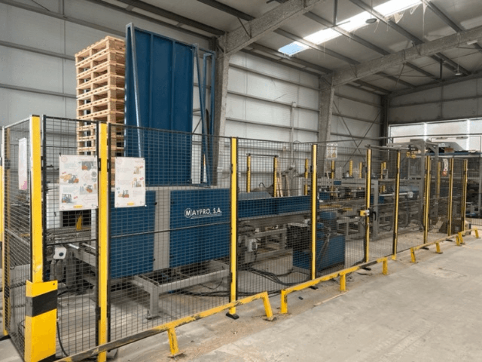 Macchina industriale per l'imballaggio di pallet di Maypro S.A. in un magazzino, con rete di sicurezza e comandi operativi, vista laterale.
