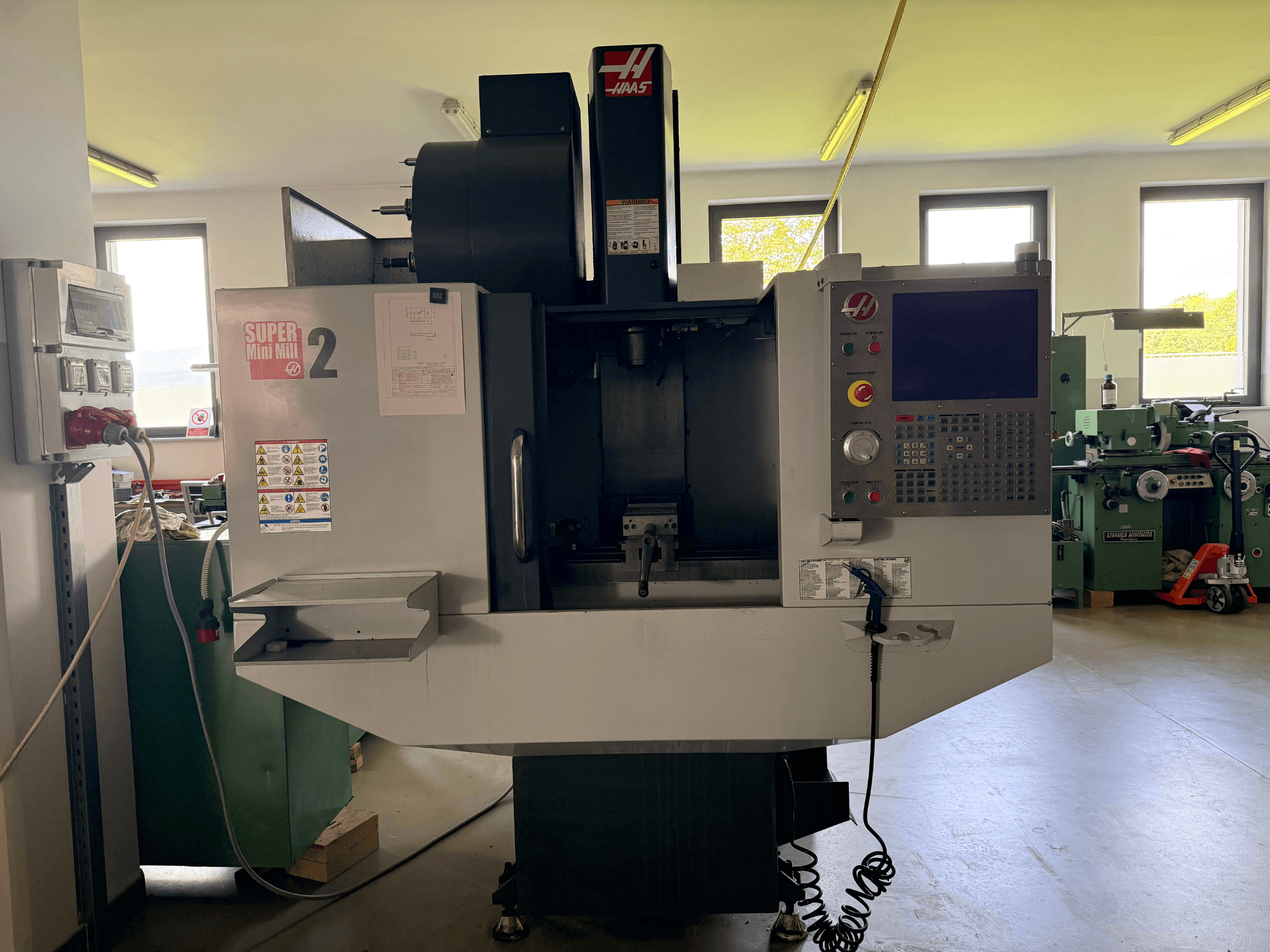 Centro di lavoro verticale Haas Mini Mill 2 in vista frontale, che mostra il pannello di controllo e l'area degli utensili con le etichette di avvertenza.