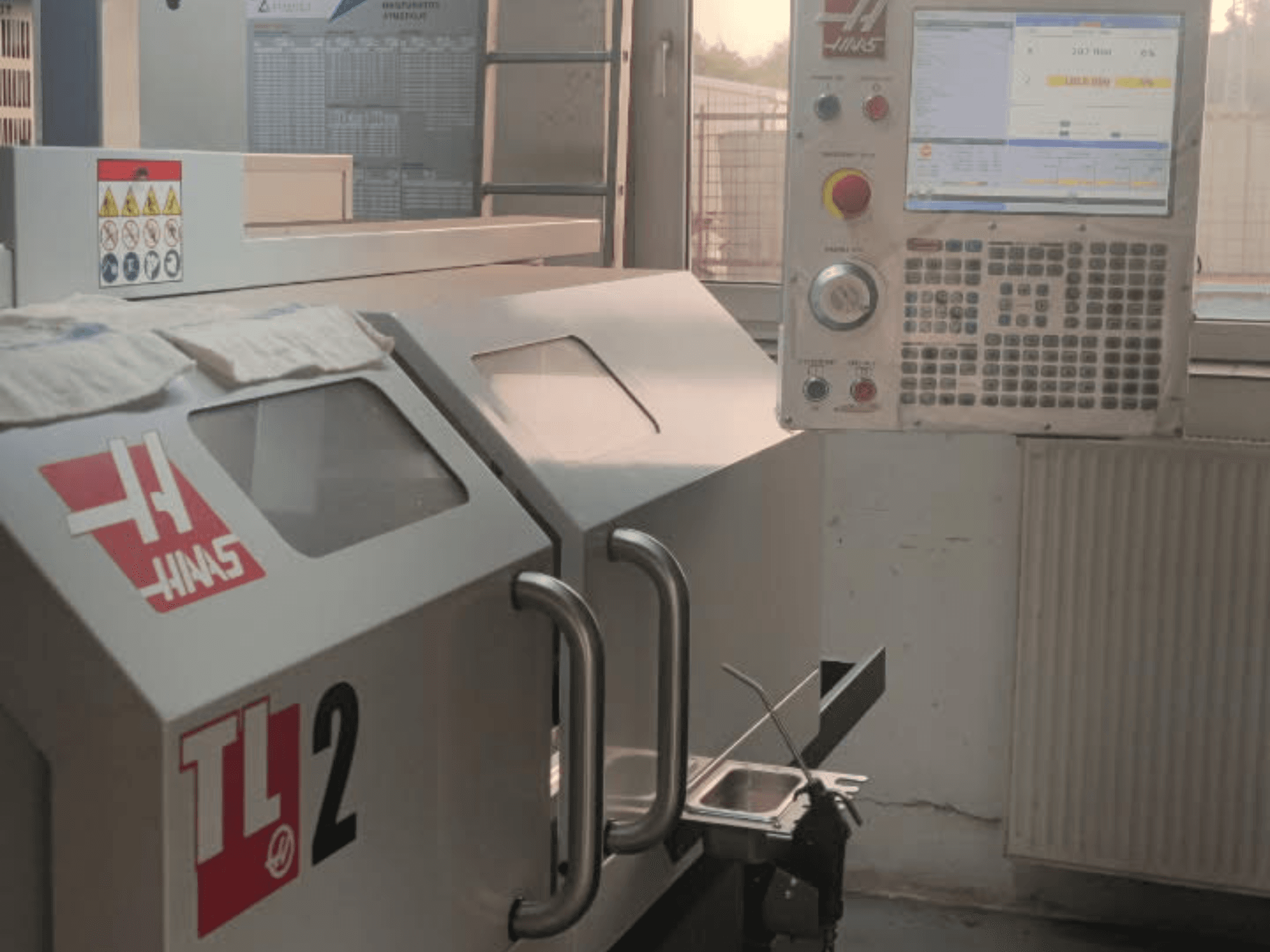 Vista frontale del tornio orizzontale Haas TL-2, con pannello di controllo, involucro metallico e segnaletica di sicurezza.