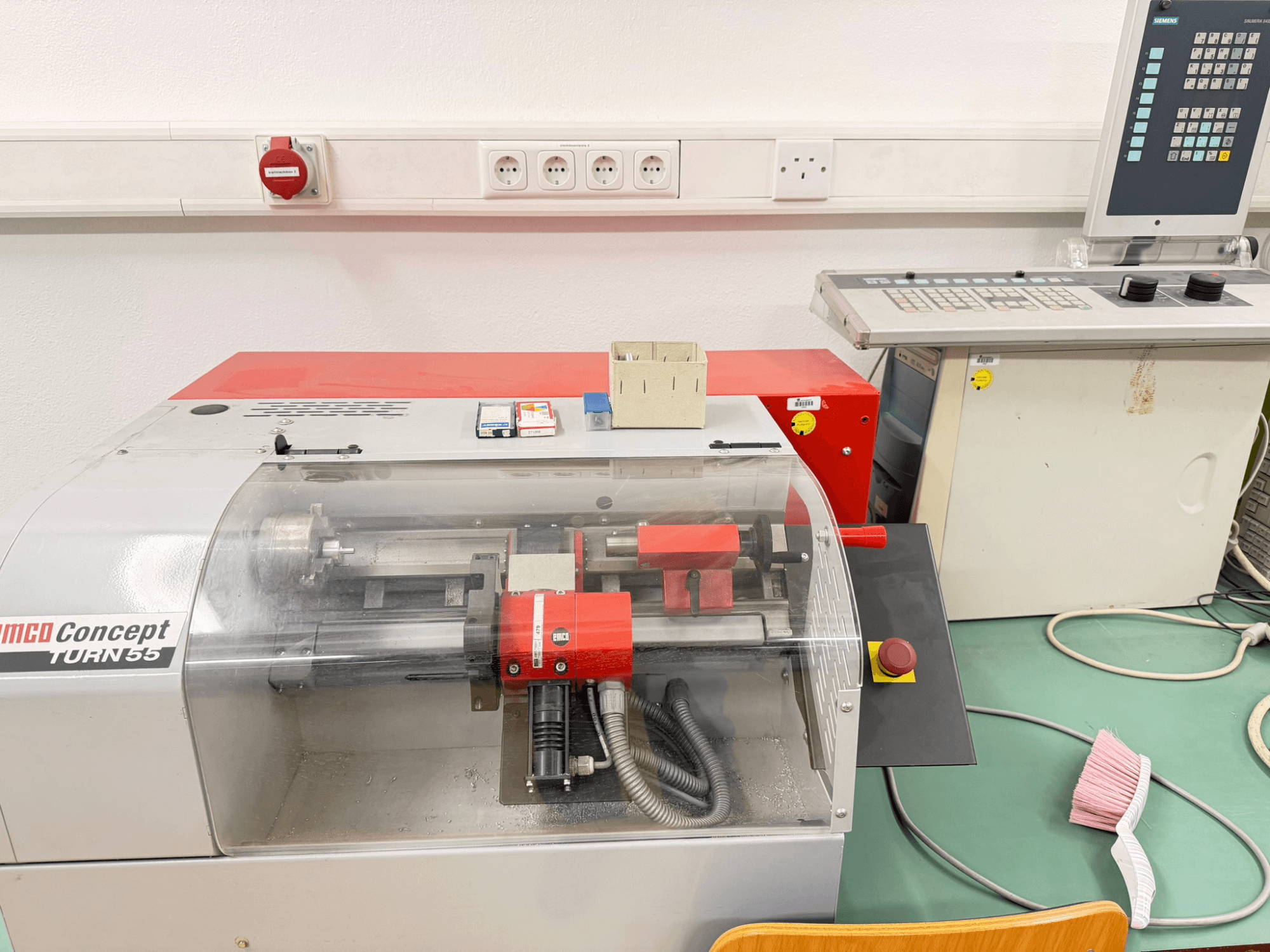 Tornio orizzontale EMCO Concept Turn 55 con esterno rosso e grigio, vista frontale che mostra i comandi e l'area di lavoro.
