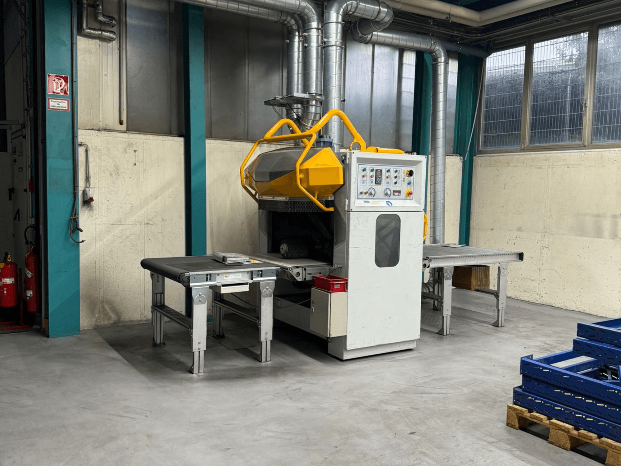 Sbavatrice Fladder AUT-1000 VAC in un ambiente di fabbrica, con pannello di controllo, protezione di sicurezza gialla e tavoli di lavoro adiacenti.