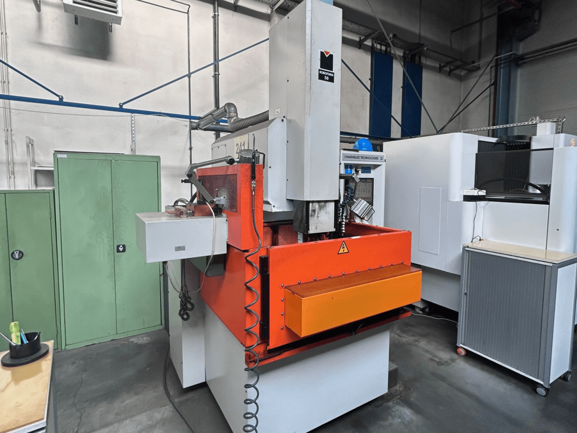 Vista frontale della macchina per elettroerosione a tuffo CHARMILLES ROBOFORM 50 con pannello arancione, interfaccia di controllo e attrezzature circostanti.