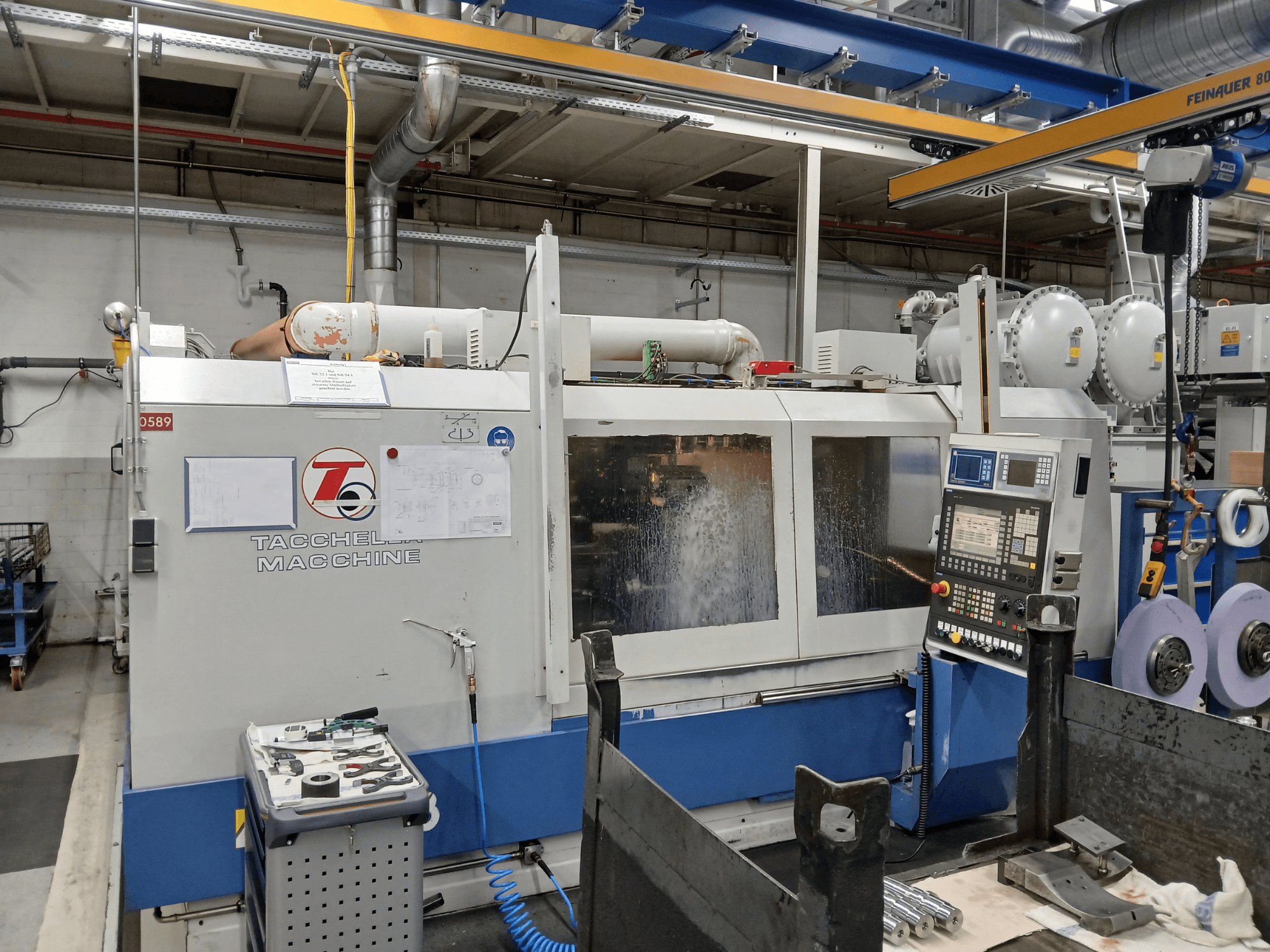 Centro di lavoro Tacchella visto frontalmente, con pannello di controllo e utensili visibili. Spruzzi di refrigerante ad acqua durante il funzionamento.