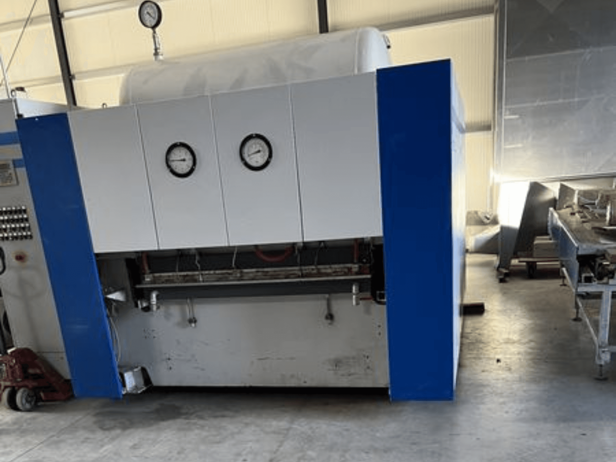 Macchina industriale blu e bianca con due manometri, vista frontale, con pannello di controllo e attrezzature adiacenti.