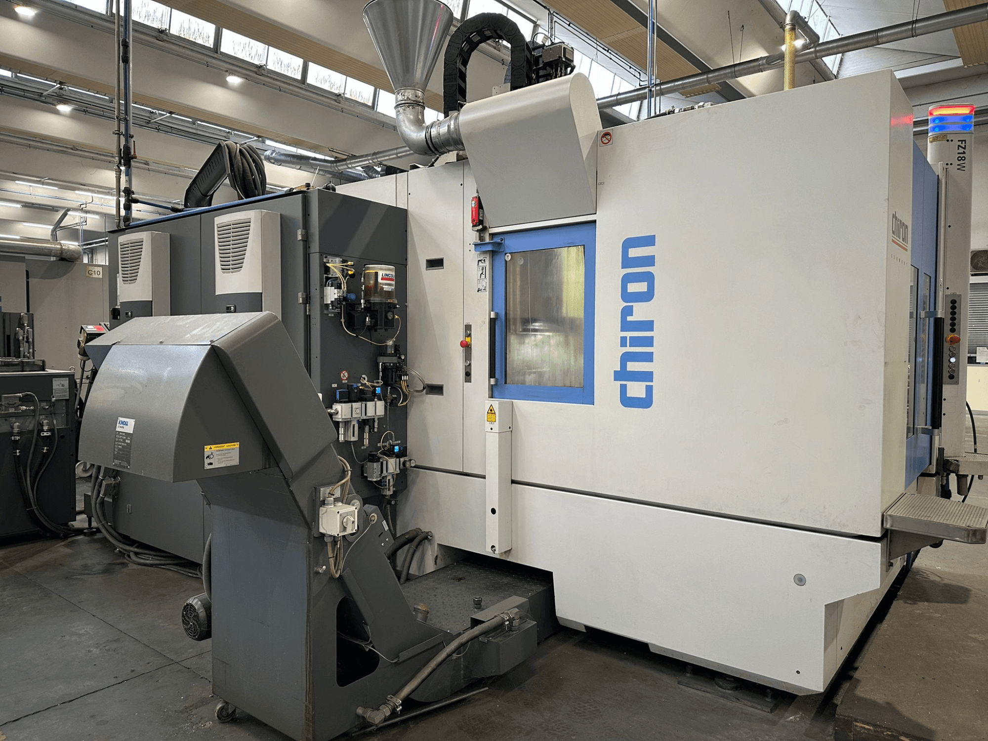 Macchina CNC Chiron in grigio e bianco, vista frontale, con comandi, tubi e cappa di aspirazione.