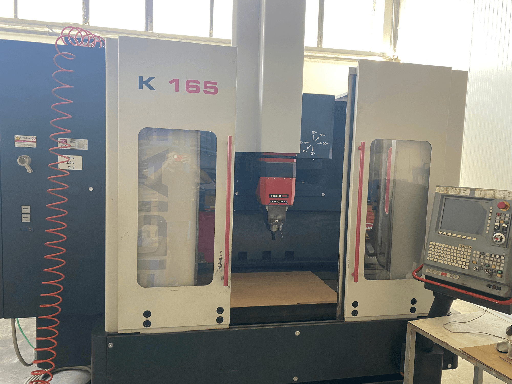Macchina CNC Fidia K 165 con mandrino e pannello di controllo rossi, vista frontalmente, in un'officina ben illuminata.