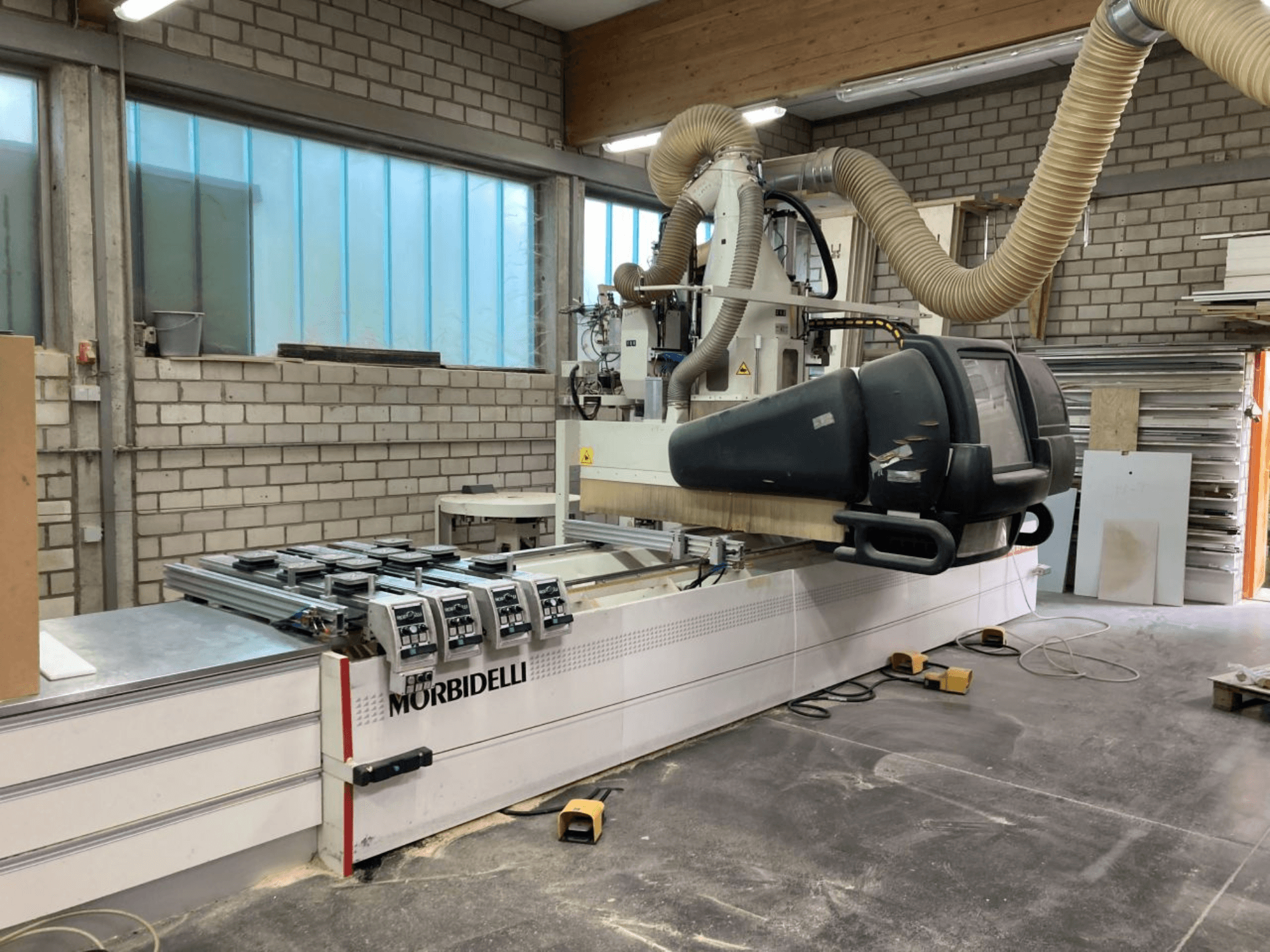 Macchina a controllo numerico MORBIDELLI in officina, vista frontale con pannello di controllo, sistema di aspirazione delle polveri e pezzo di legno posizionato.