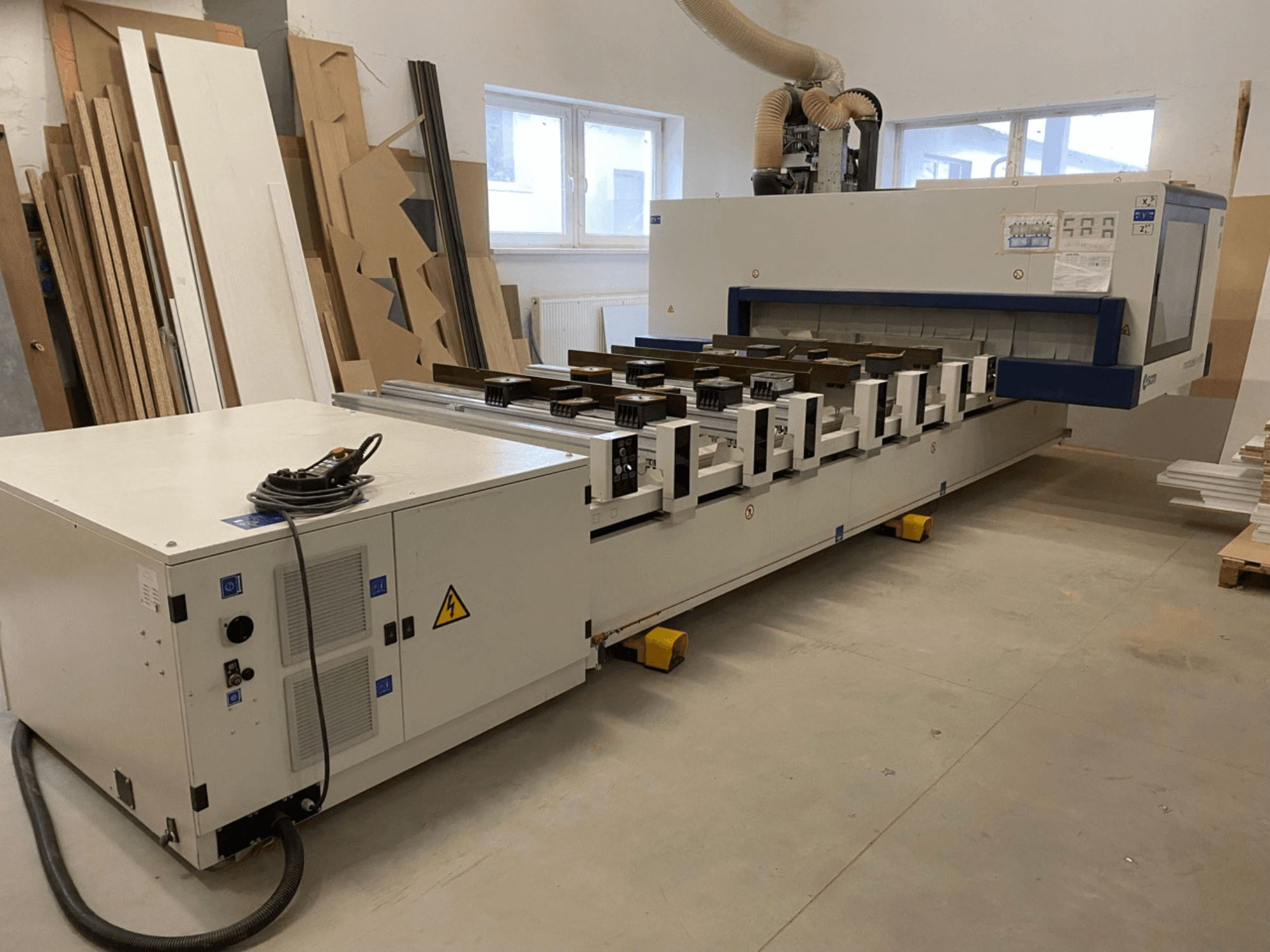 Centro di lavorazione del legno a controllo numerico SCM Morbidelli modello M100 in un'officina, con vista frontale che mostra il pannello di comando e il sistema di aspirazione della polvere.