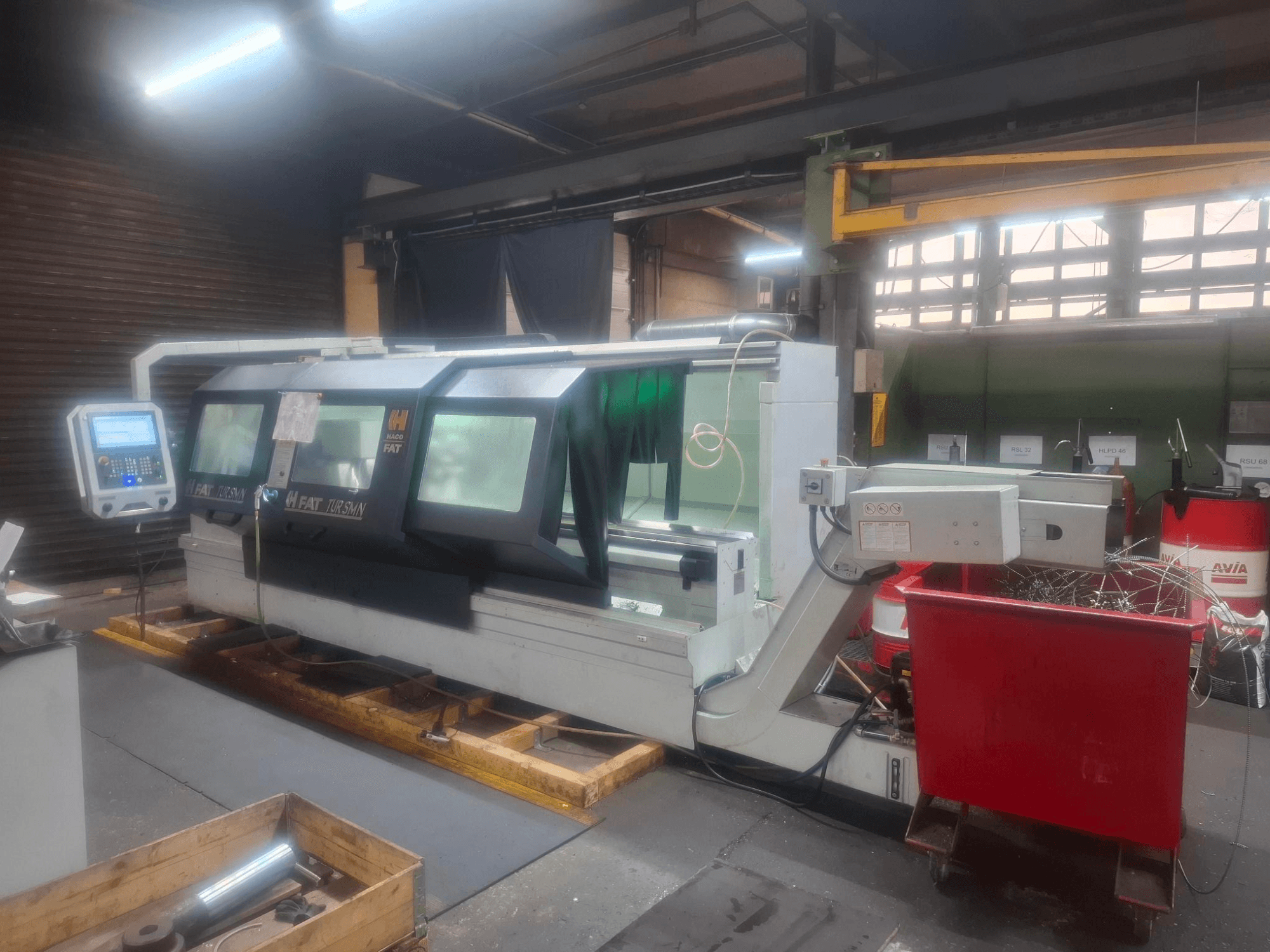 Vista frontale di una macchina CNC FAT Tursan con pannello di controllo, posizionata su pallet di legno in un'officina.