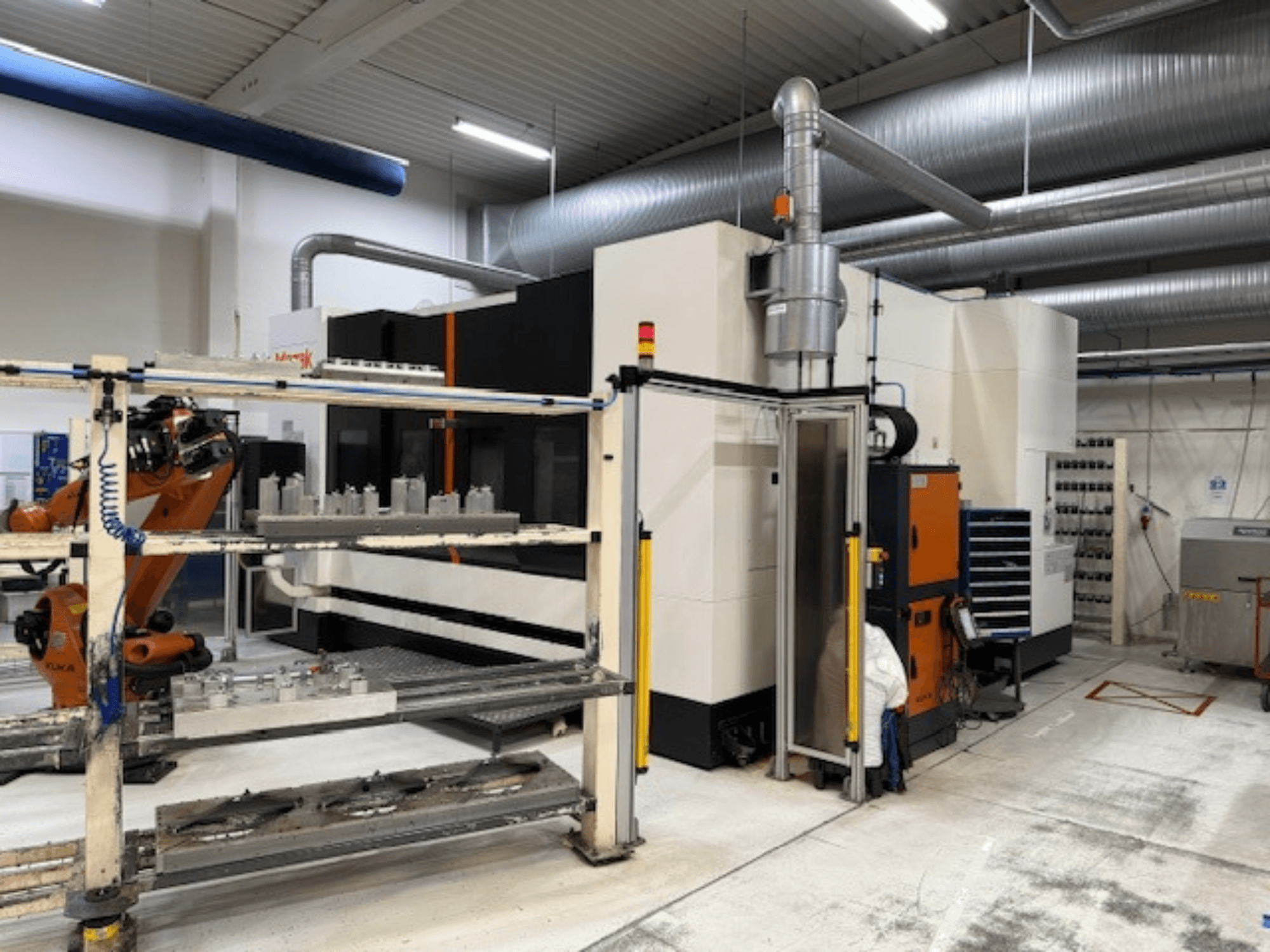 Macchina CNC industriale con braccio robotico e barriere di sicurezza, con vista frontale dell'installazione in un'area di lavoro ariosa.