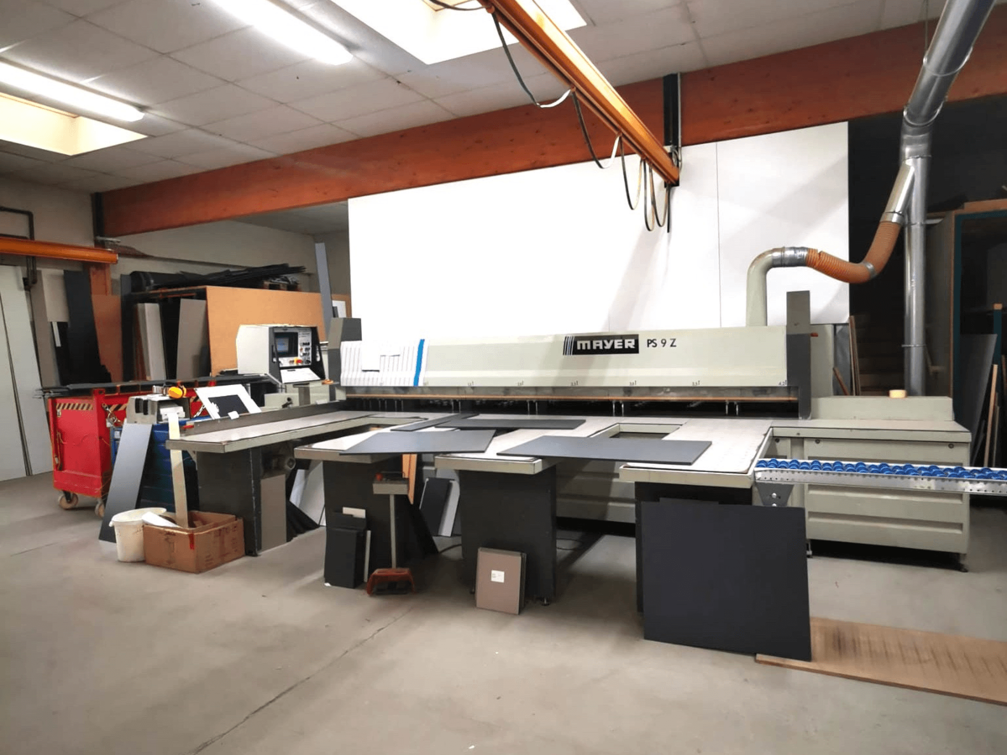 Macchina da taglio MAYER PS9 Z in un'officina, vista frontale, con vari materiali e un sistema di trasporto visibile.
