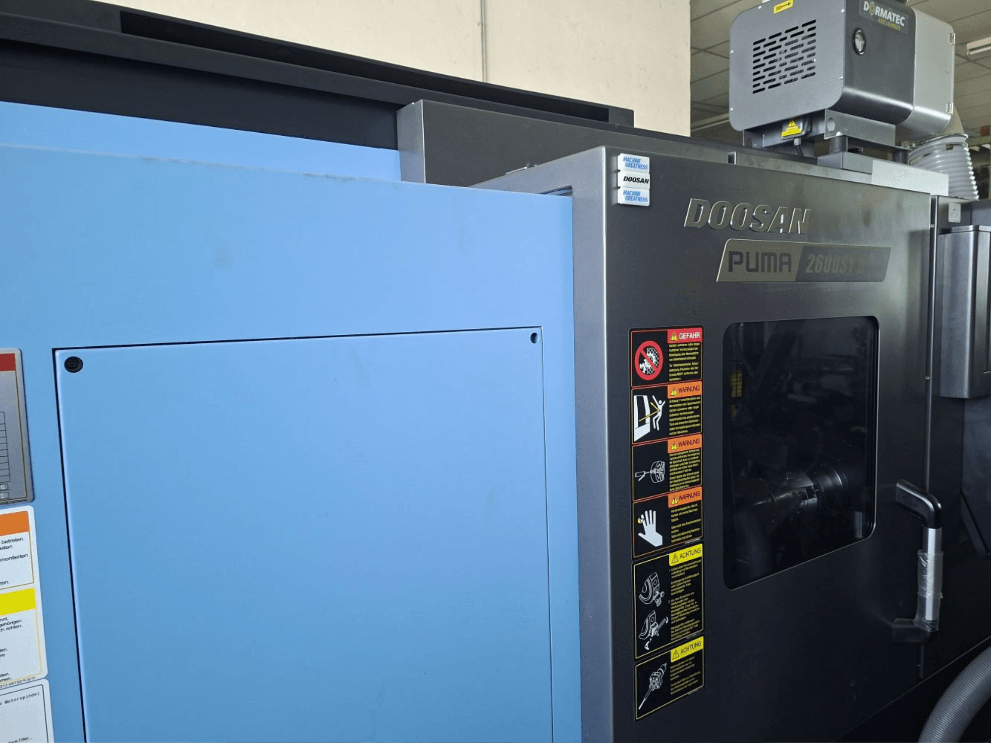 Tornio orizzontale DOOSAN PUMA 2600 SY II, vista frontale, con etichette di sicurezza e pannelli blu.