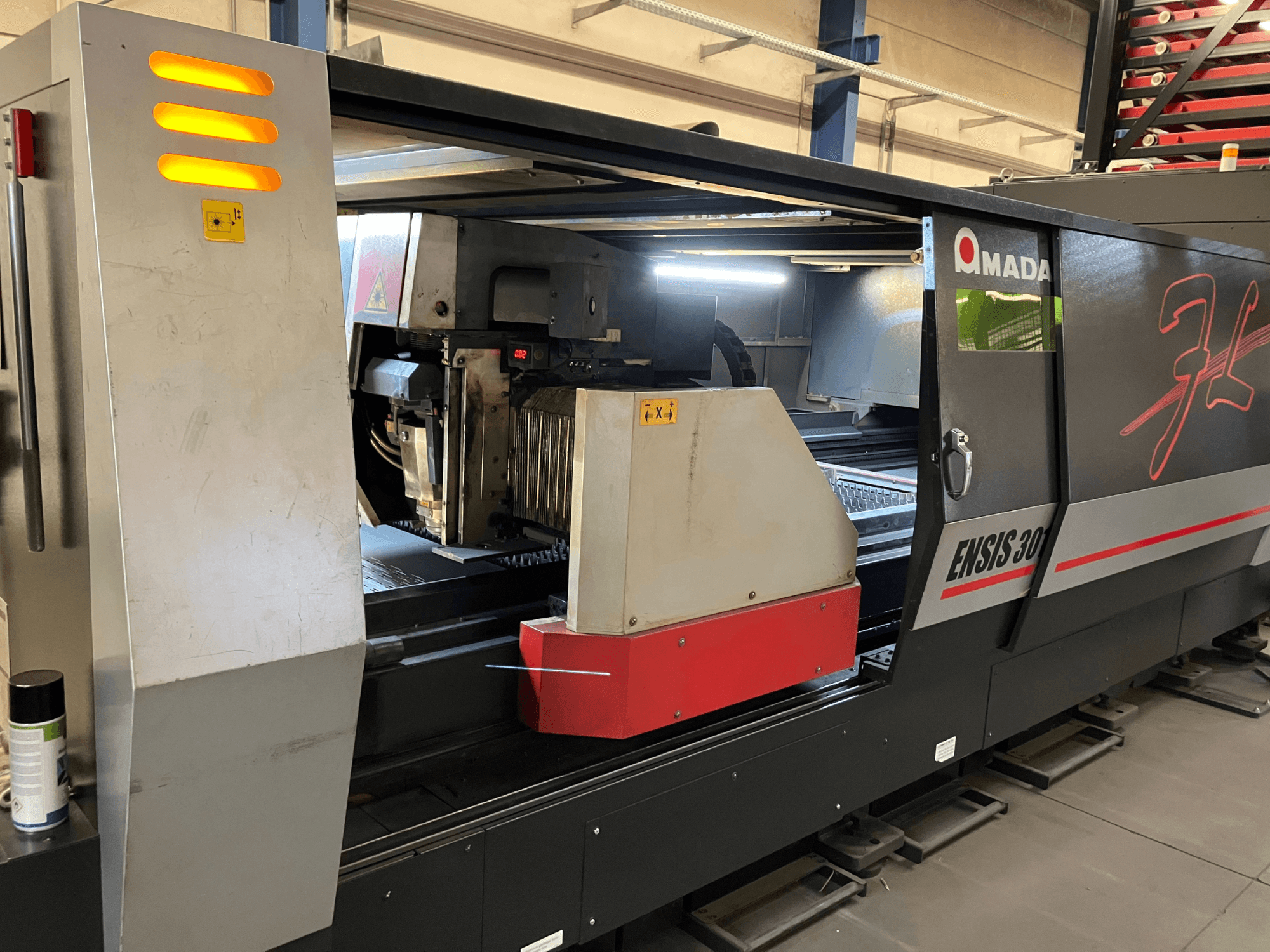 Macchina per il taglio laser in fibra AMADA ENSIS 3015 AJ, vista frontale, che mostra la testa di taglio e i comandi operativi all'interno di un telaio metallico.