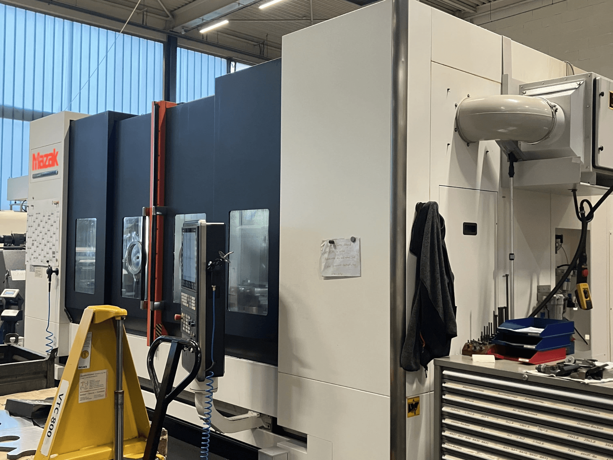 Macchina CNC Mazak vista di lato, che mostra il pannello di controllo e le caratteristiche di sicurezza in un ambiente di officina.