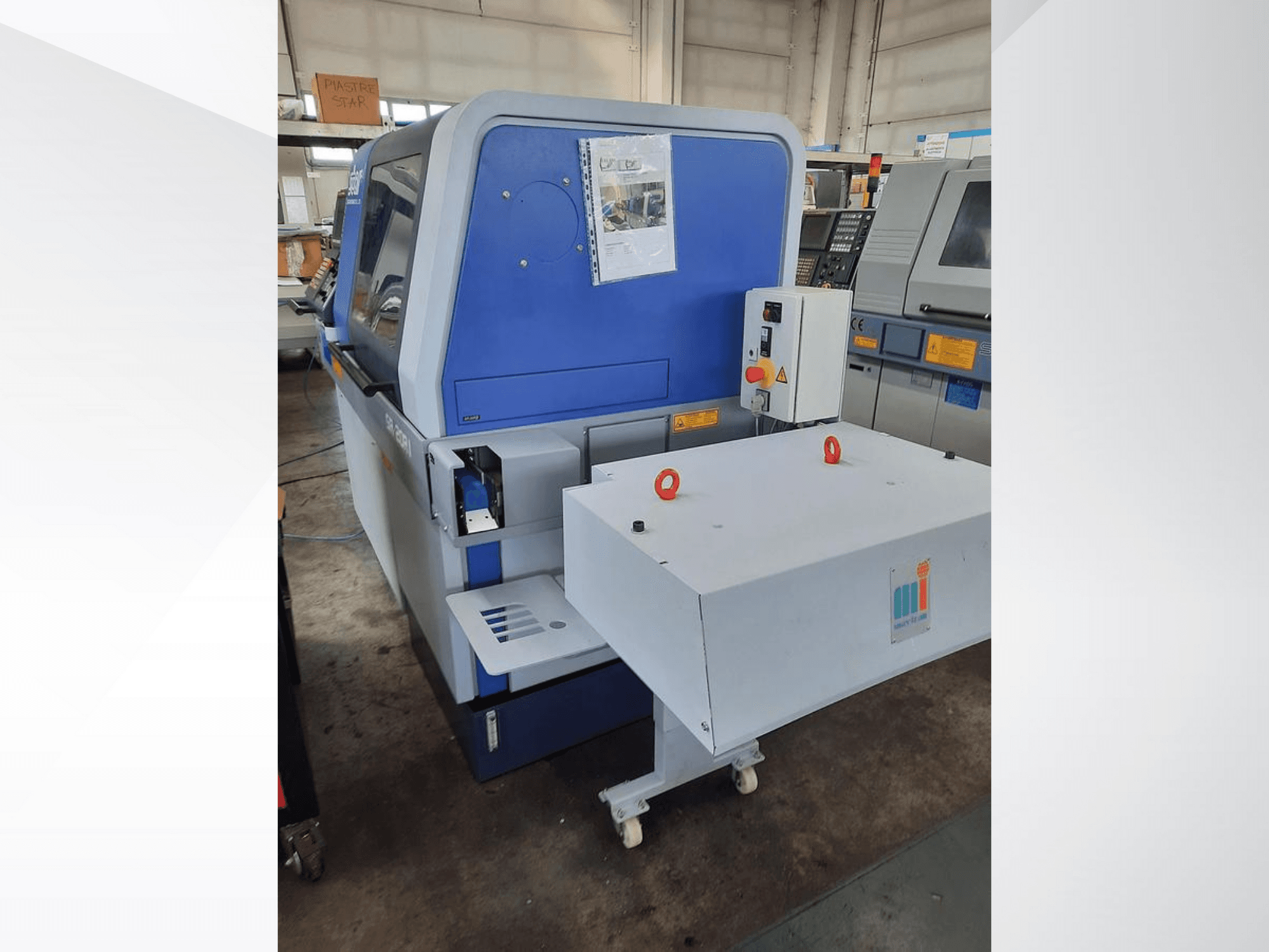 Macchina industriale blu con nastro trasportatore bianco, che mostra il pannello di controllo e i dispositivi di sicurezza annessi, vista laterale.